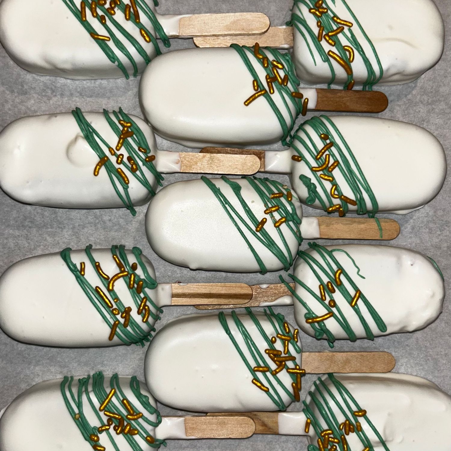 White chocolate cake pops decorated with green stripes and gold accents arranged in rows.