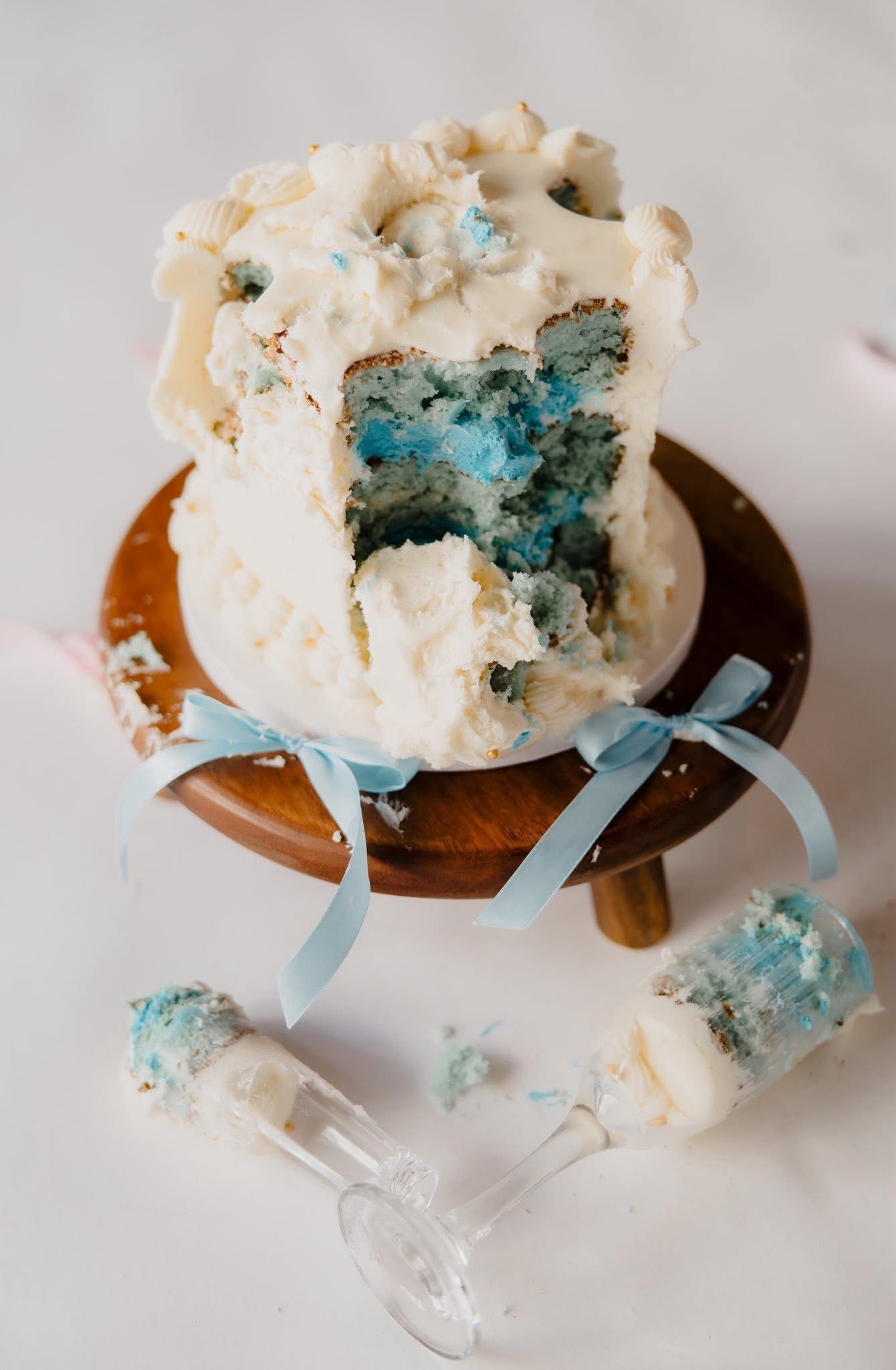 A gender reveal cake with white frosting reveals blue filling as it's cut open, showing it's a boy.
