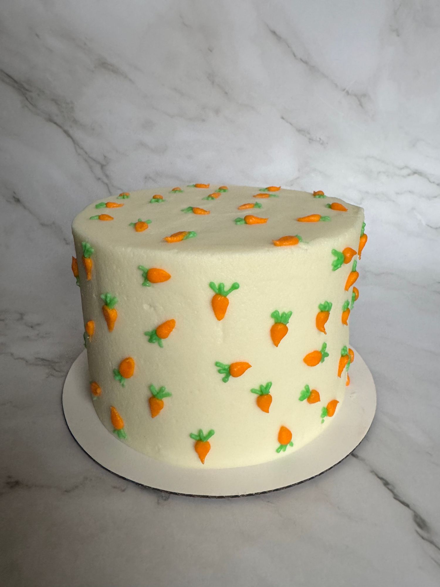 White round cake decorated with small orange carrots and green tops in a repeating pattern.