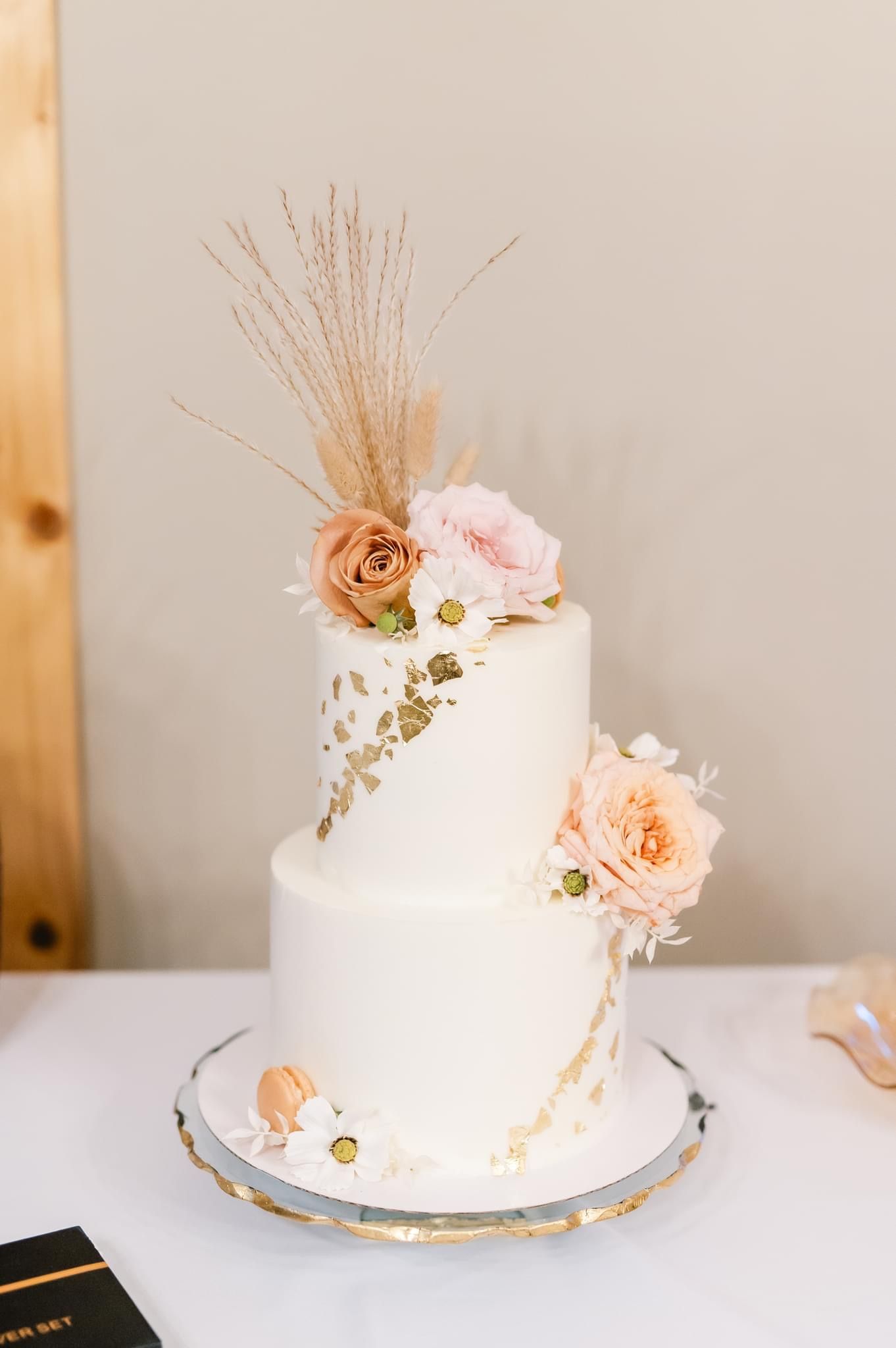 Elegant white wedding cake adorned with delicate peach roses and floral accents on a silver cake stand.
