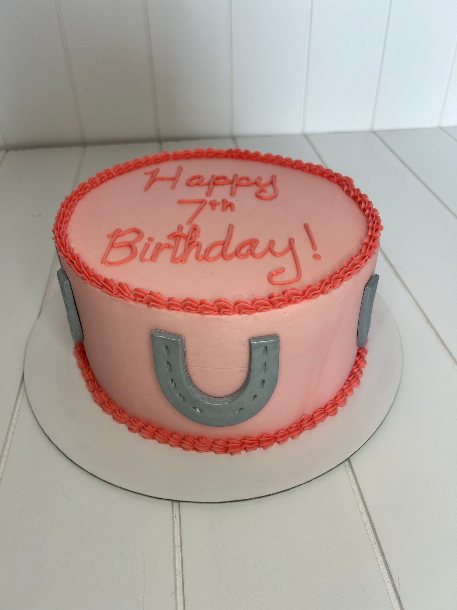 Pink birthday cake with horseshoe decoration and piped border details.