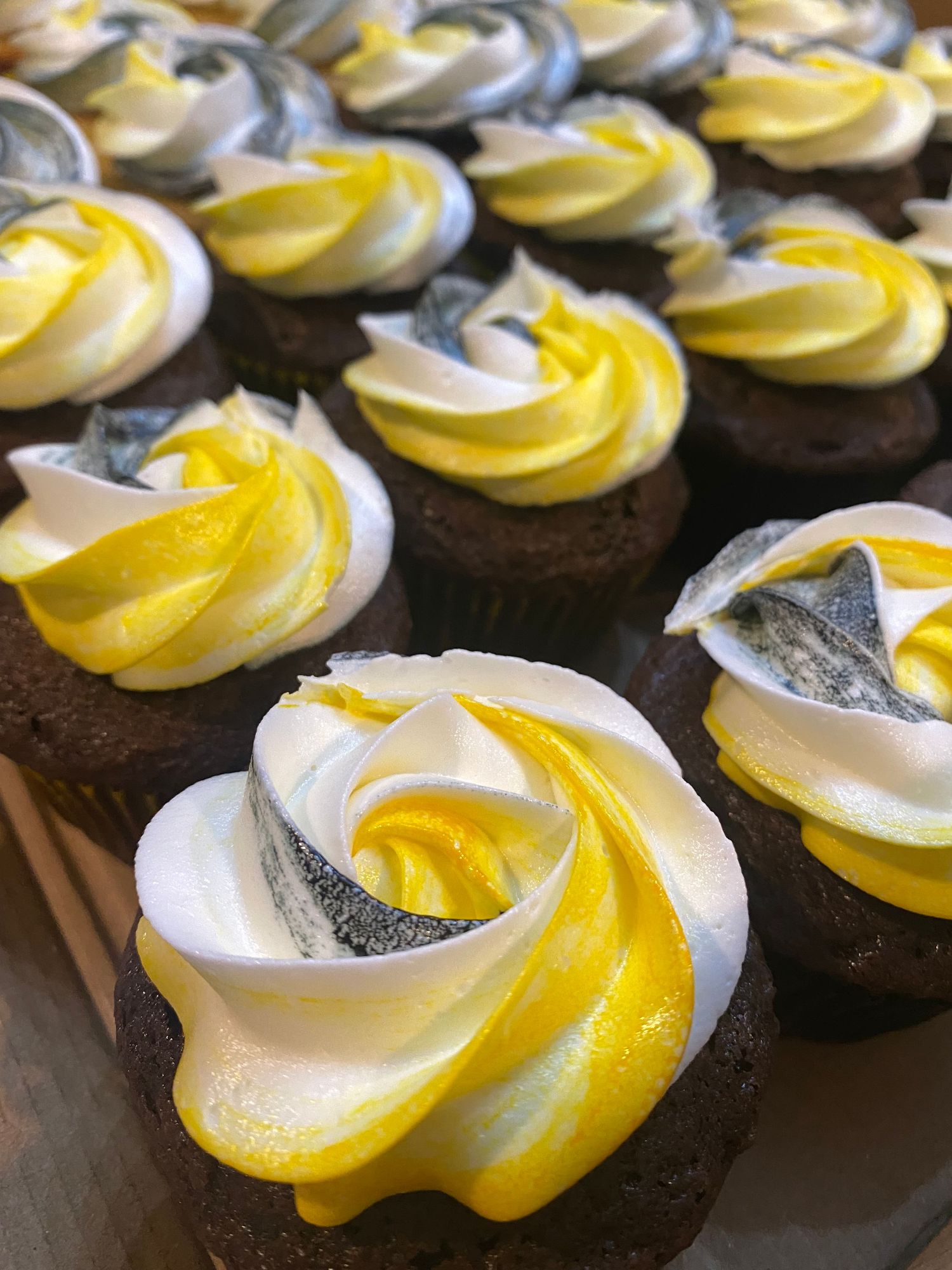 Chocolate cupcakes decorated with swirled yellow and white buttercream frosting in a spiral pattern.