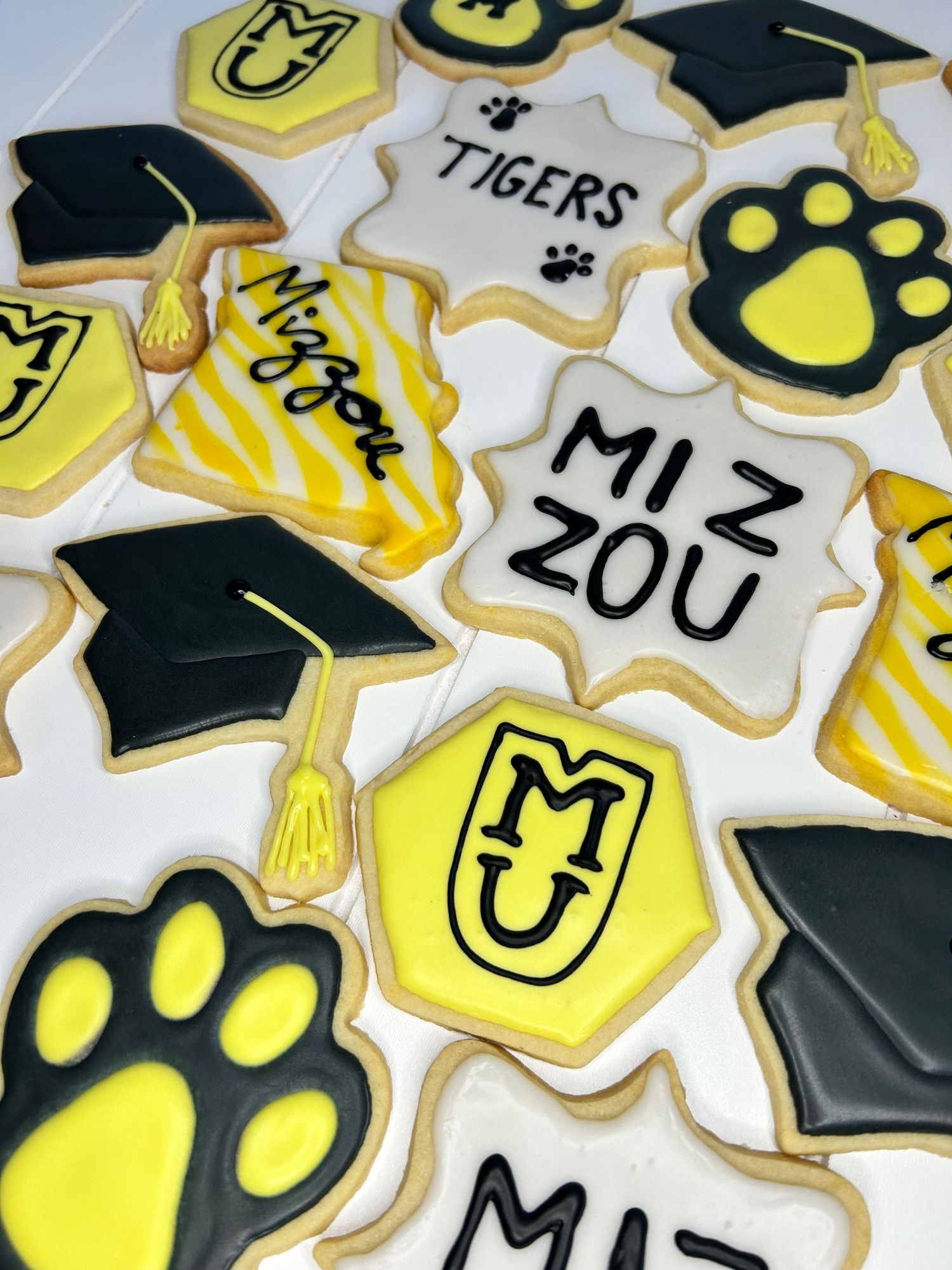 Graduation themed sugar cookies with yellow and black designs featuring caps and paw prints.
