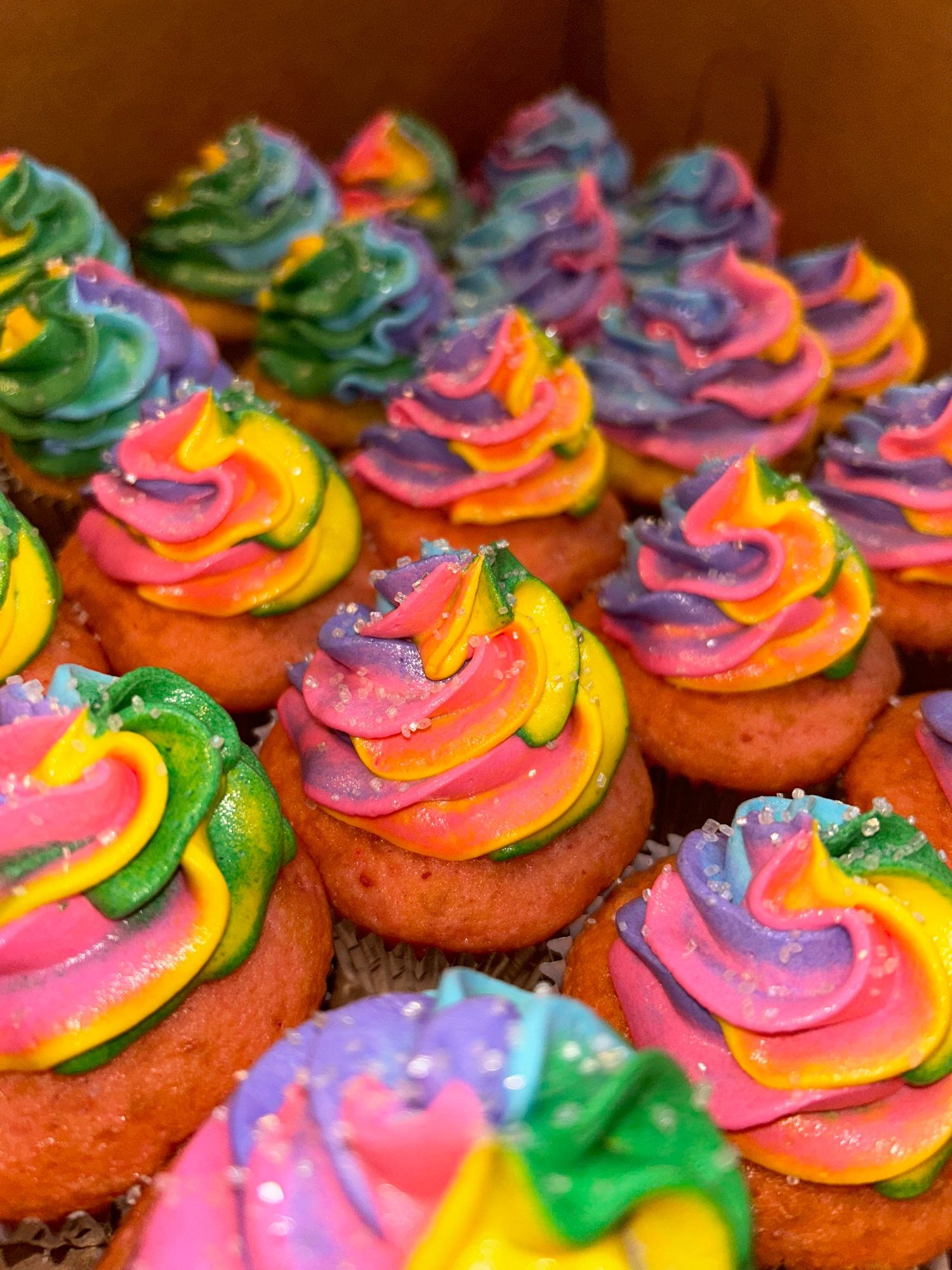Vibrant rainbow colored cupcakes with multicolored swirled frosting.