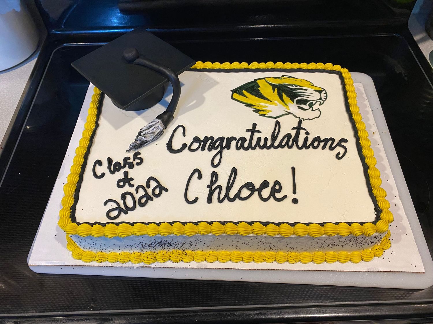 Long rectangular sheet cake with yellow trim and black text decorated in a traditional congratulatory style.