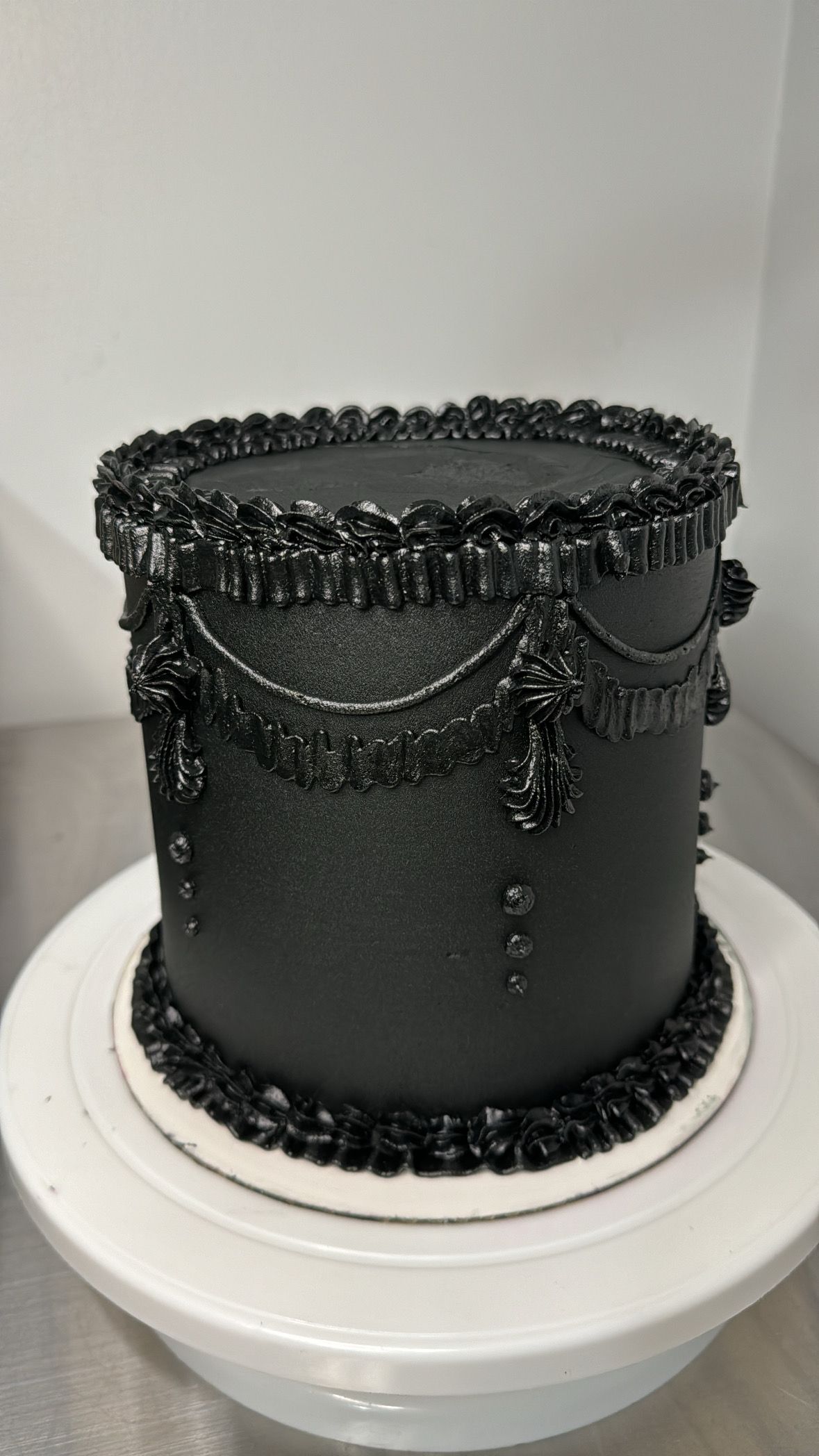 Elegant black cake with intricate piped lace details and Victorian-style decorative border.
