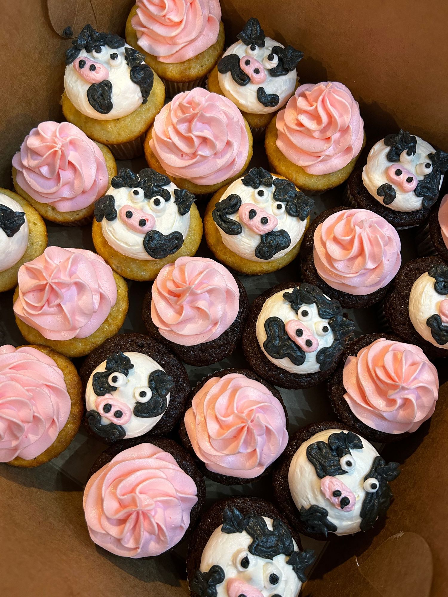 Cupcakes decorated with pink frosting and black and white cow face designs.