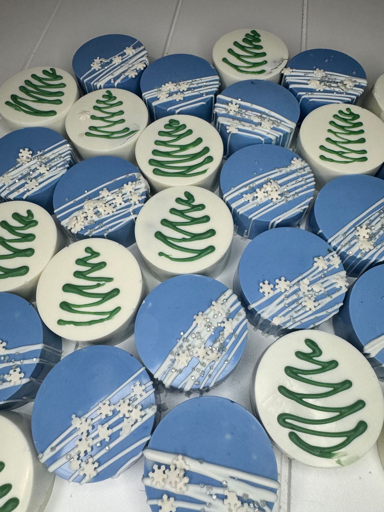 Winter-themed chocolate covered Oreos decorated with snowflakes and Christmas trees in blue and white.