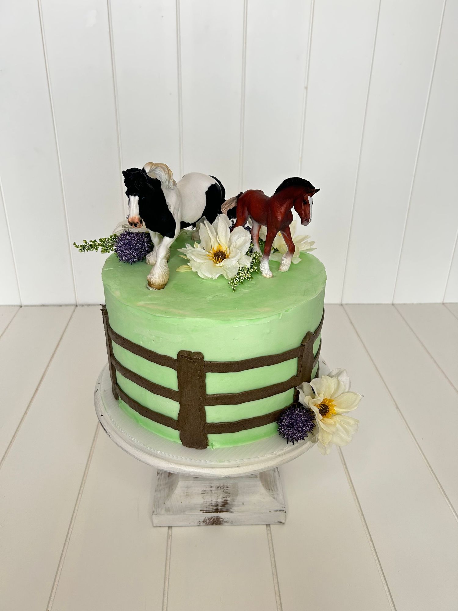 A mint green cake decorated with horse figures, daisies, and a fence design around the sides.