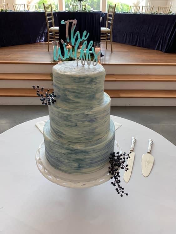 Modern blue marbled wedding cake with turquoise topper on white display table.