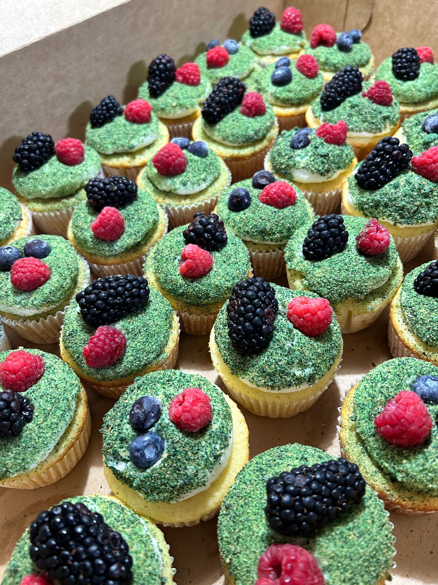 Green frosted cupcakes topped with fresh blackberries and raspberries.