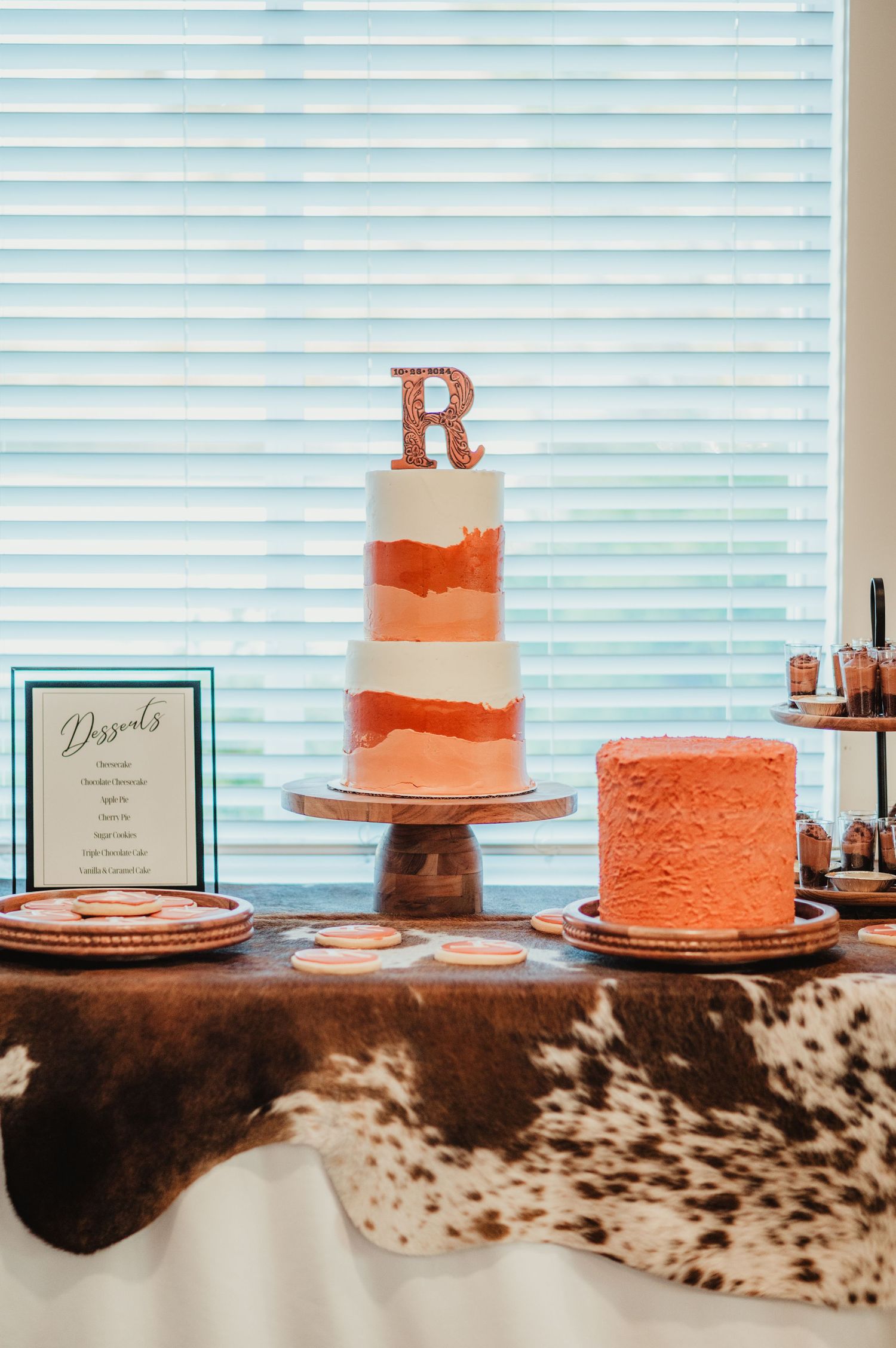 Coral colored wedding cakes displayed on a table with cowhide decor.
