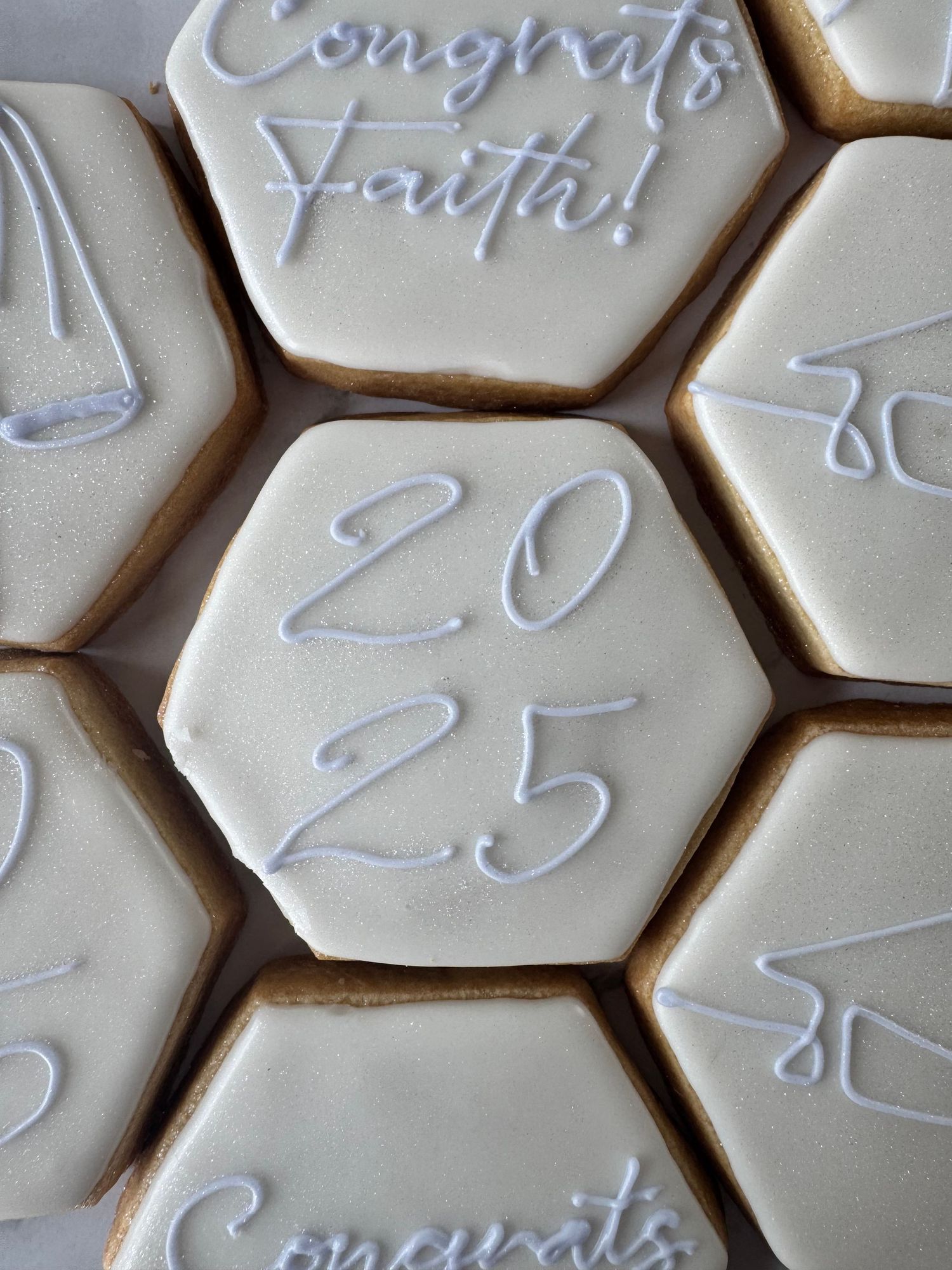 Close-up of hexagonal sugar cookies with white icing and delicate cursive text decorations.