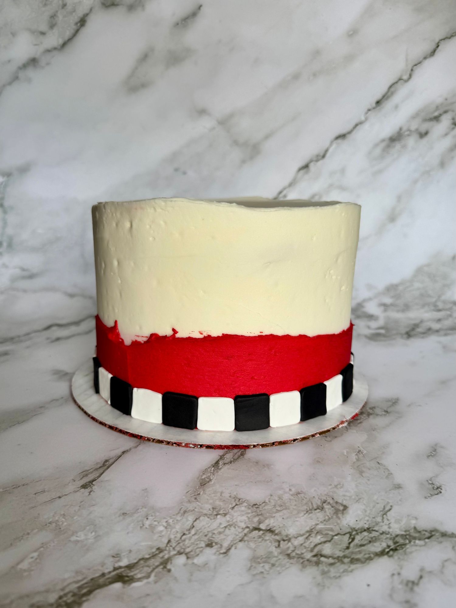 White frosted cake with red band and black and white checkered border pattern.