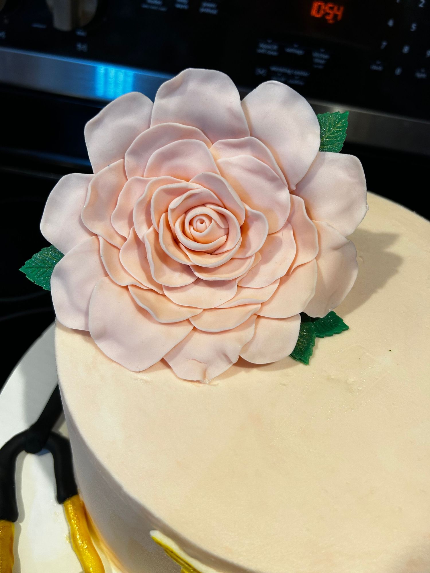 Elegant pink fondant rose decoration with green leaves on a light colored cake.