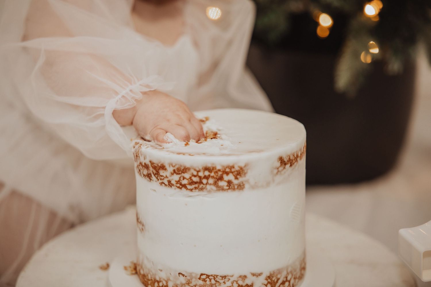 A tiered white wedding cake with gold accents and delicate floral decorations being assembled at an elegant reception.
