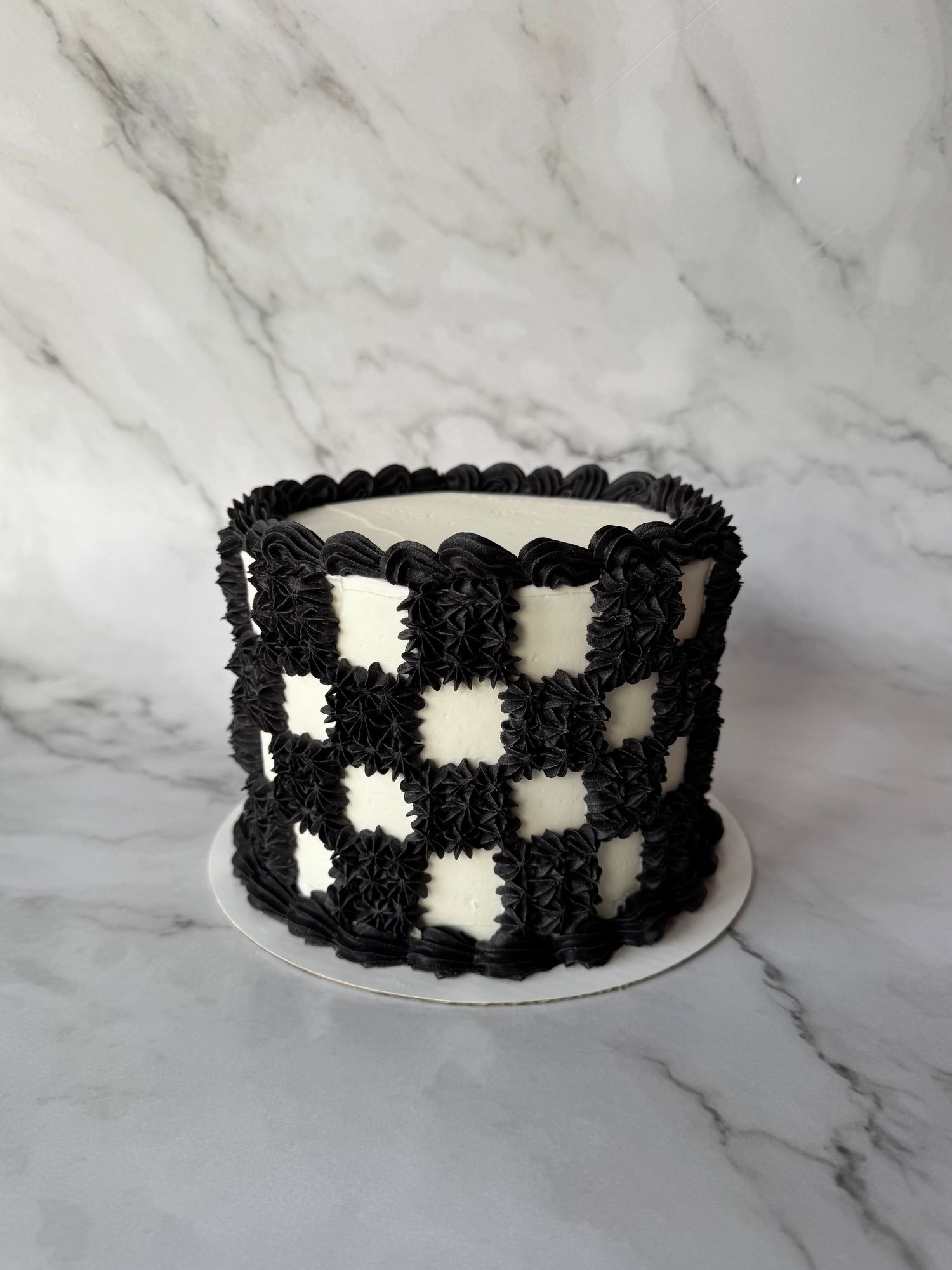 Black and white checkerboard pattern cake with textured frosting on marble surface.