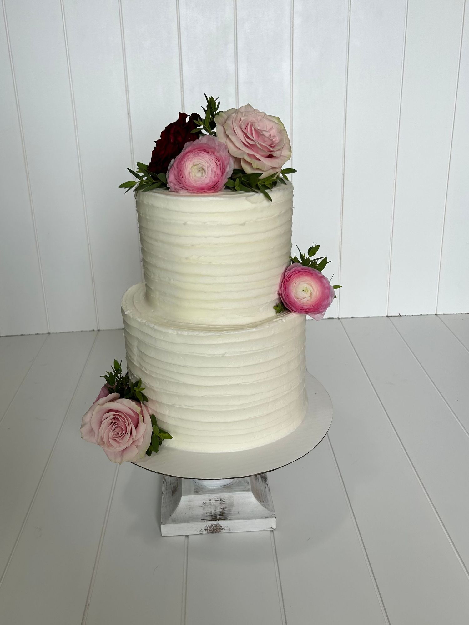 Simple white buttercream cake decorated with fresh pink roses and greenery on white background.