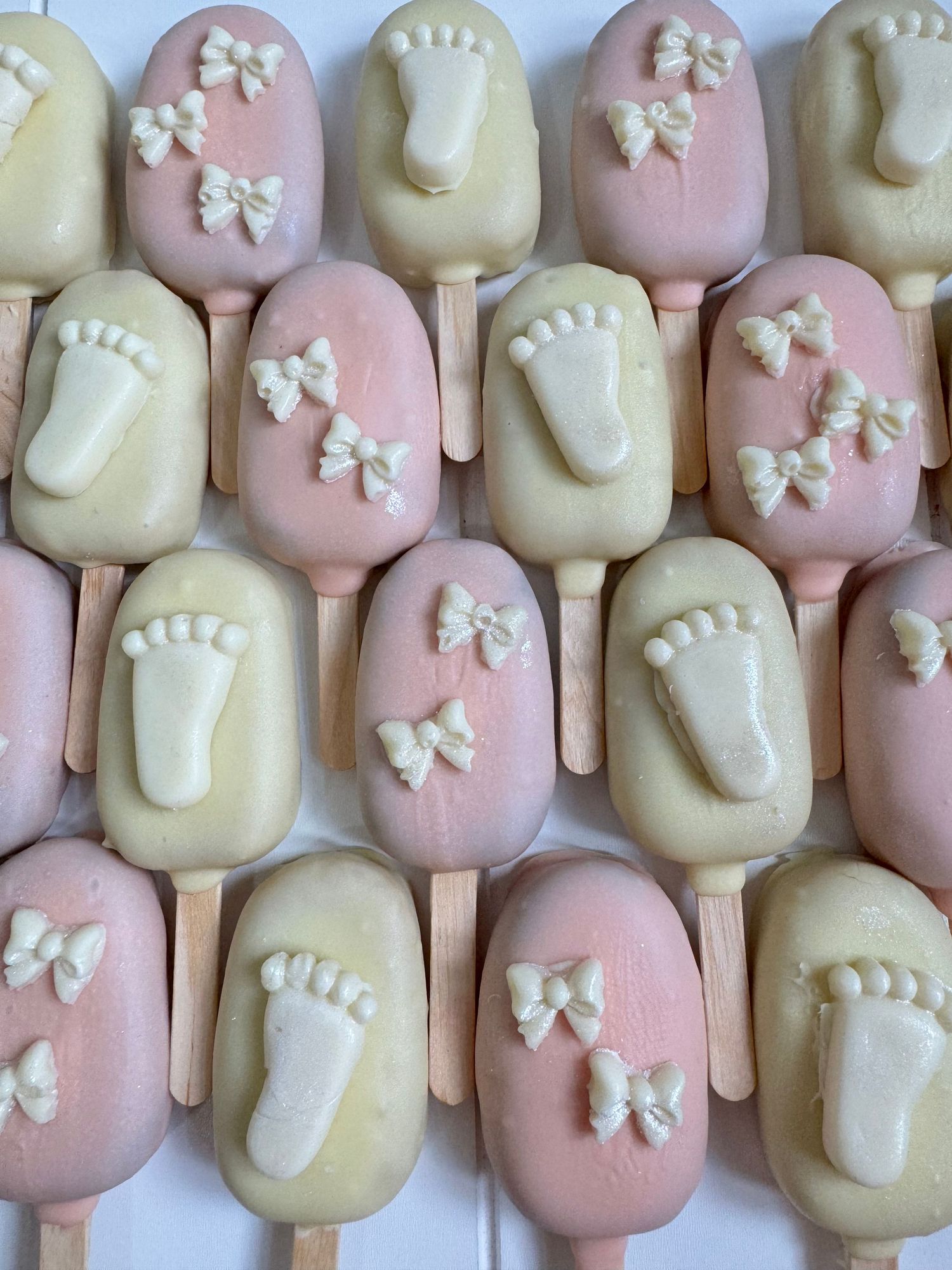 Baby shower themed cake pops decorated with bows and footprints in pink and white colors.