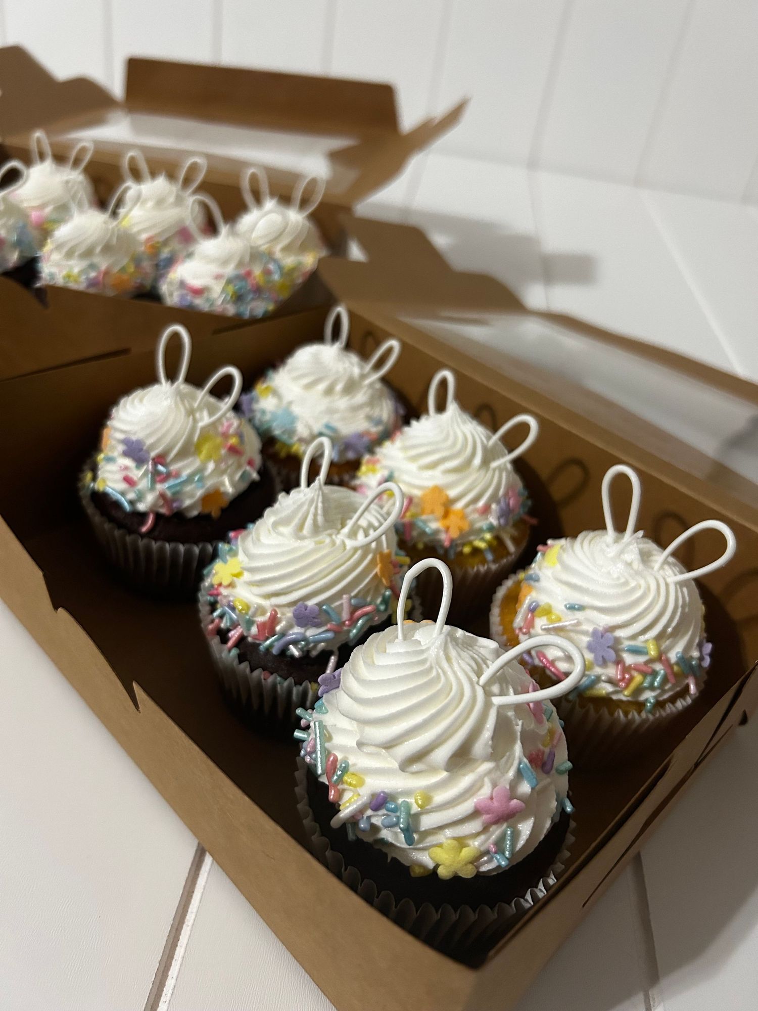 Chocolate cupcakes with white frosting and colorful sprinkles in a bakery box.