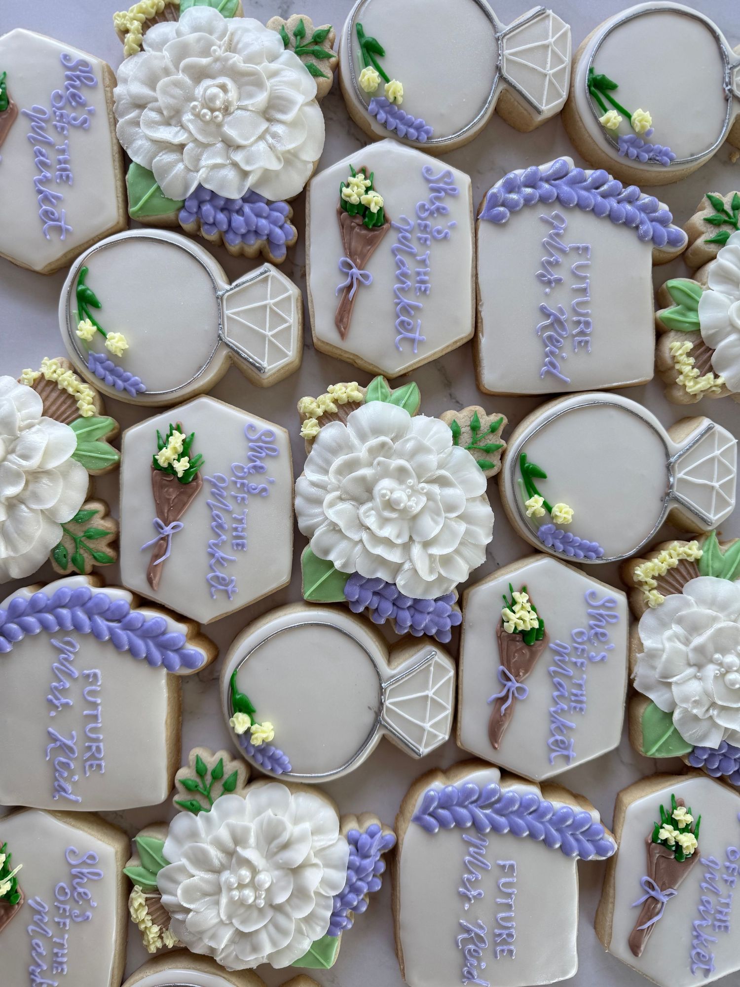 Elegant wedding cookies decorated in white and lavender with floral and geometric patterns.