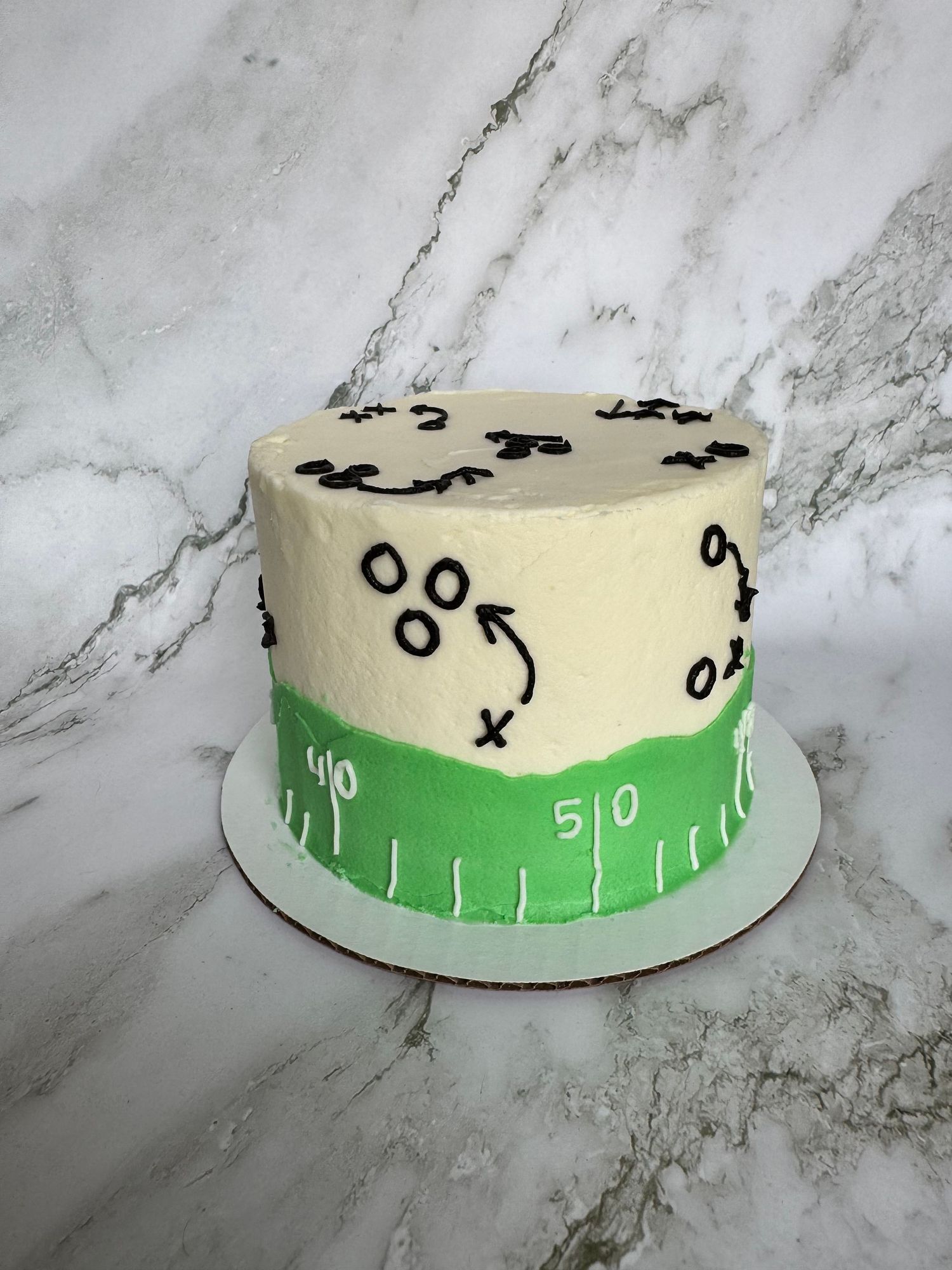 Round cake decorated with black swirls and markings on a cream base with green football field design.