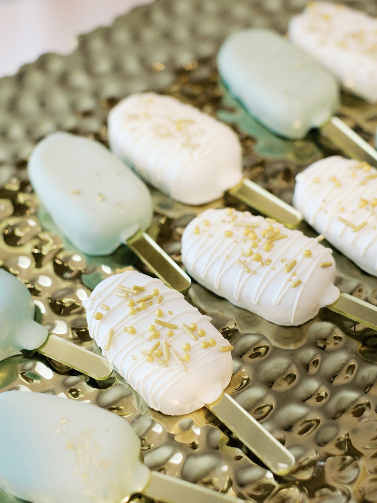 White chocolate covered desserts decorated with gold sprinkles displayed on a metallic tray.