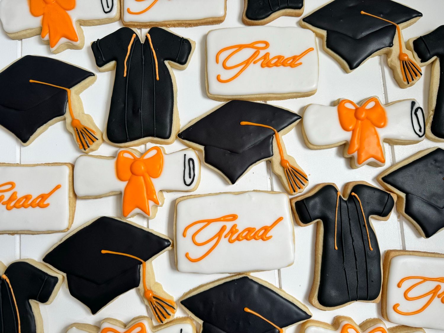 Graduation themed sugar cookies with black caps, gowns, and orange accents.