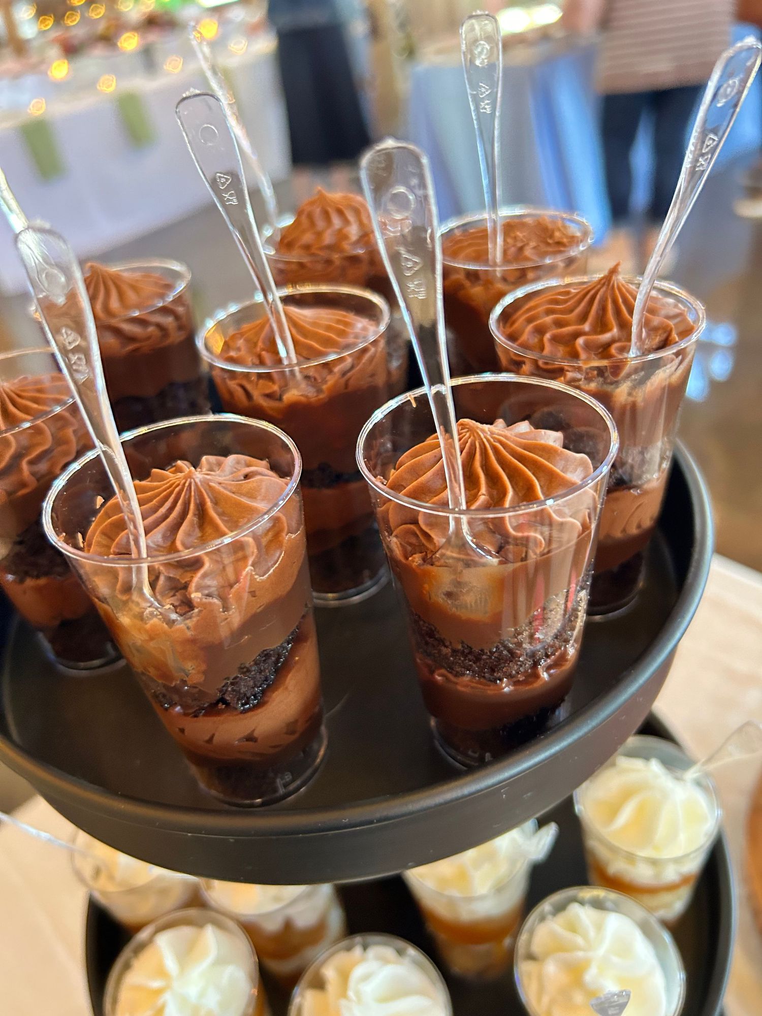 Elegant chocolate mousse desserts with whipped topping served in small glass cups on a black tiered platter.