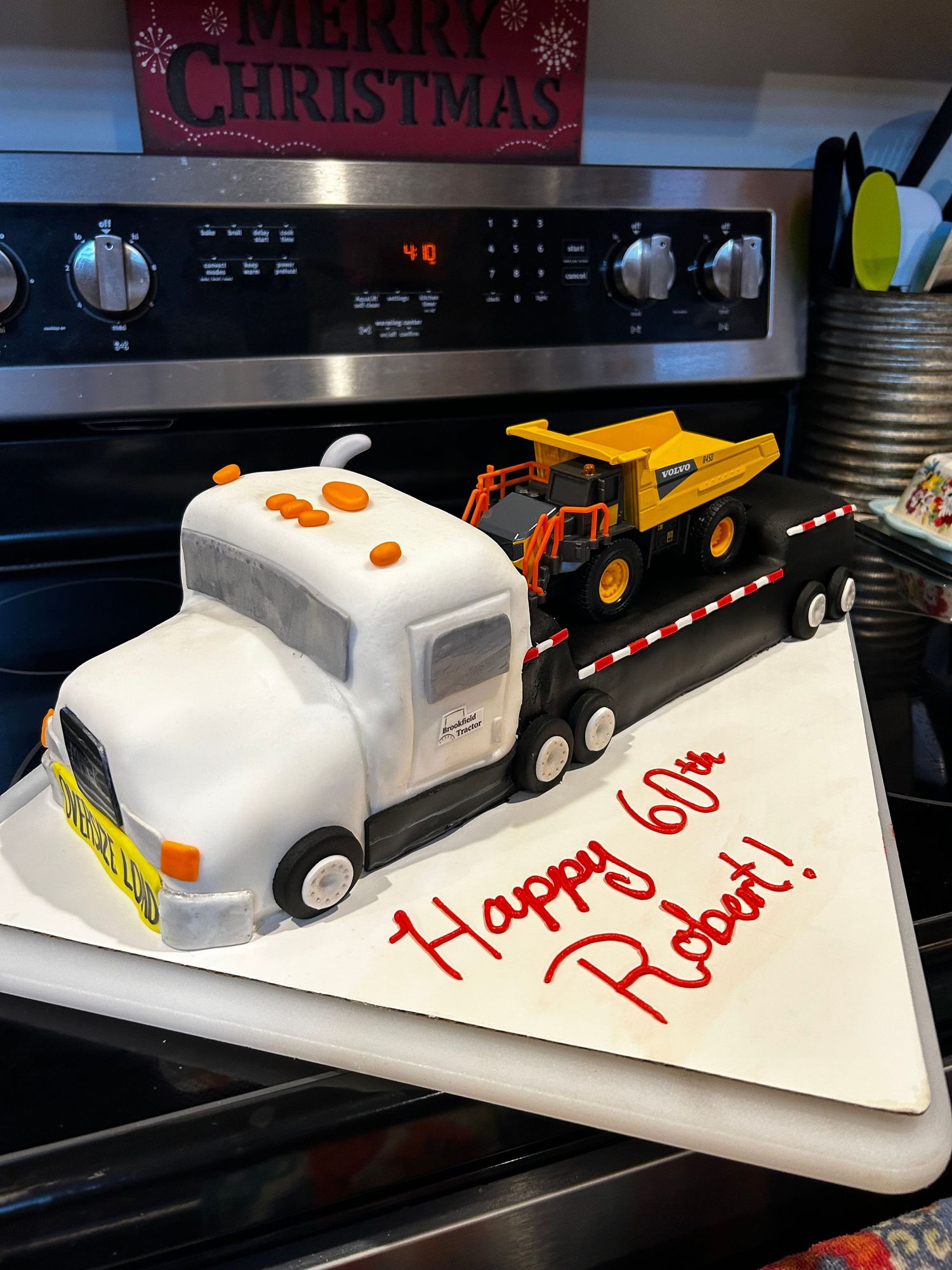 A truck-shaped cake with a yellow construction vehicle on the flatbed.