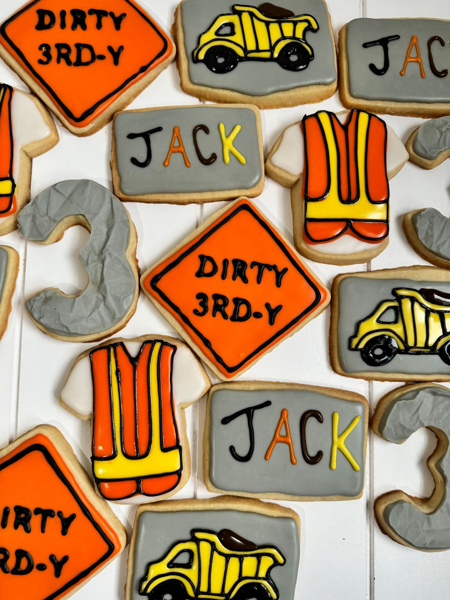Construction themed sugar cookies decorated with orange, yellow and gray icing featuring trucks and signs.