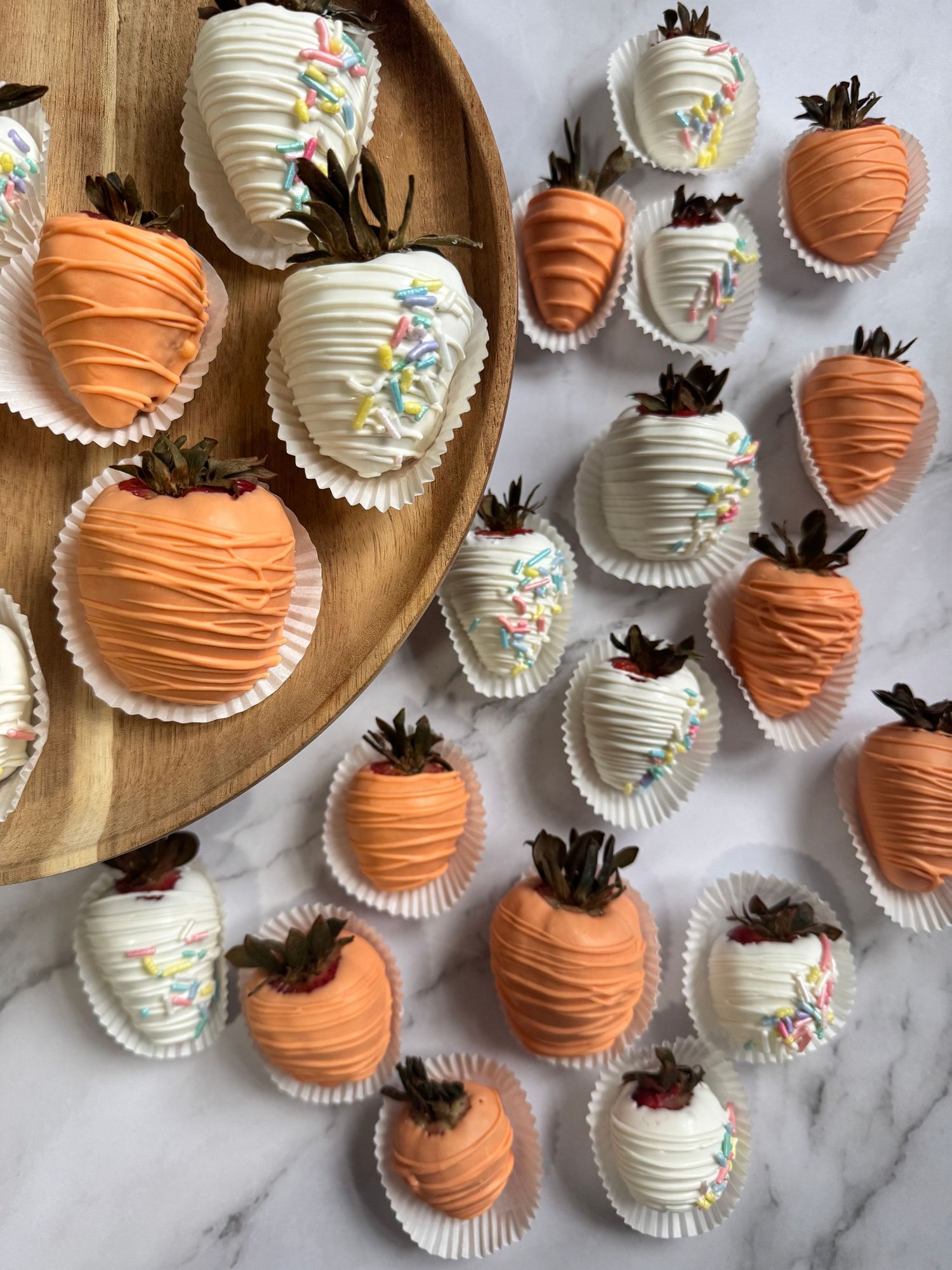 White and orange chocolate covered strawberries decorated with colorful sprinkles on a marble surface.
