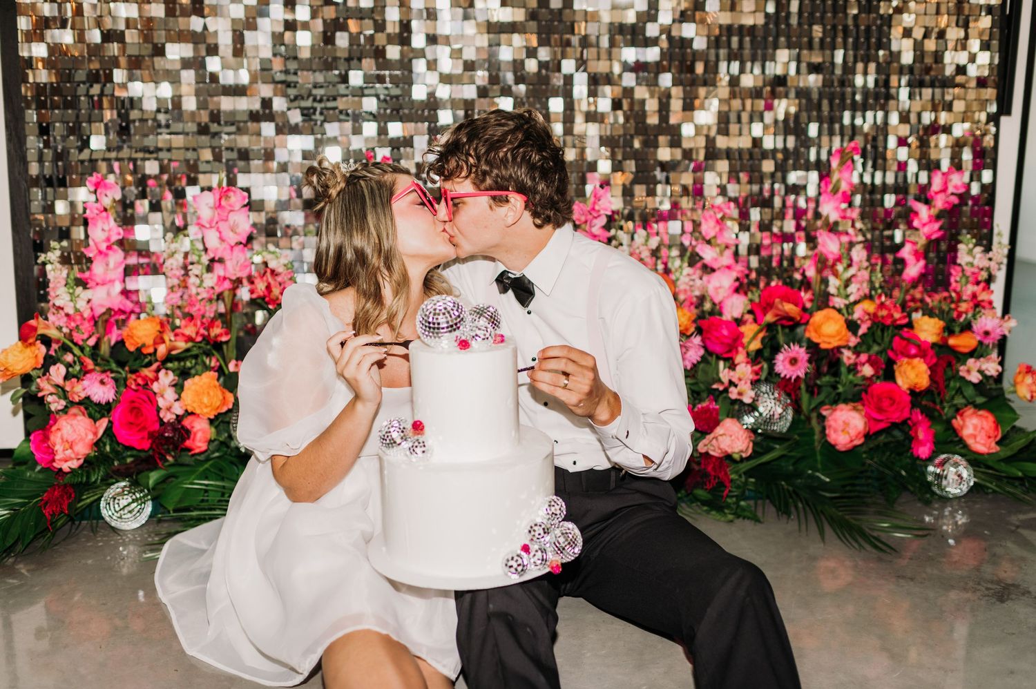 Wedding reception setup with pink floral wall backdrop and sparkly sequin decorations.