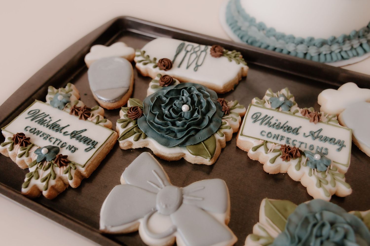 Elegant white and teal decorated cookies and desserts arranged on dark display trays.