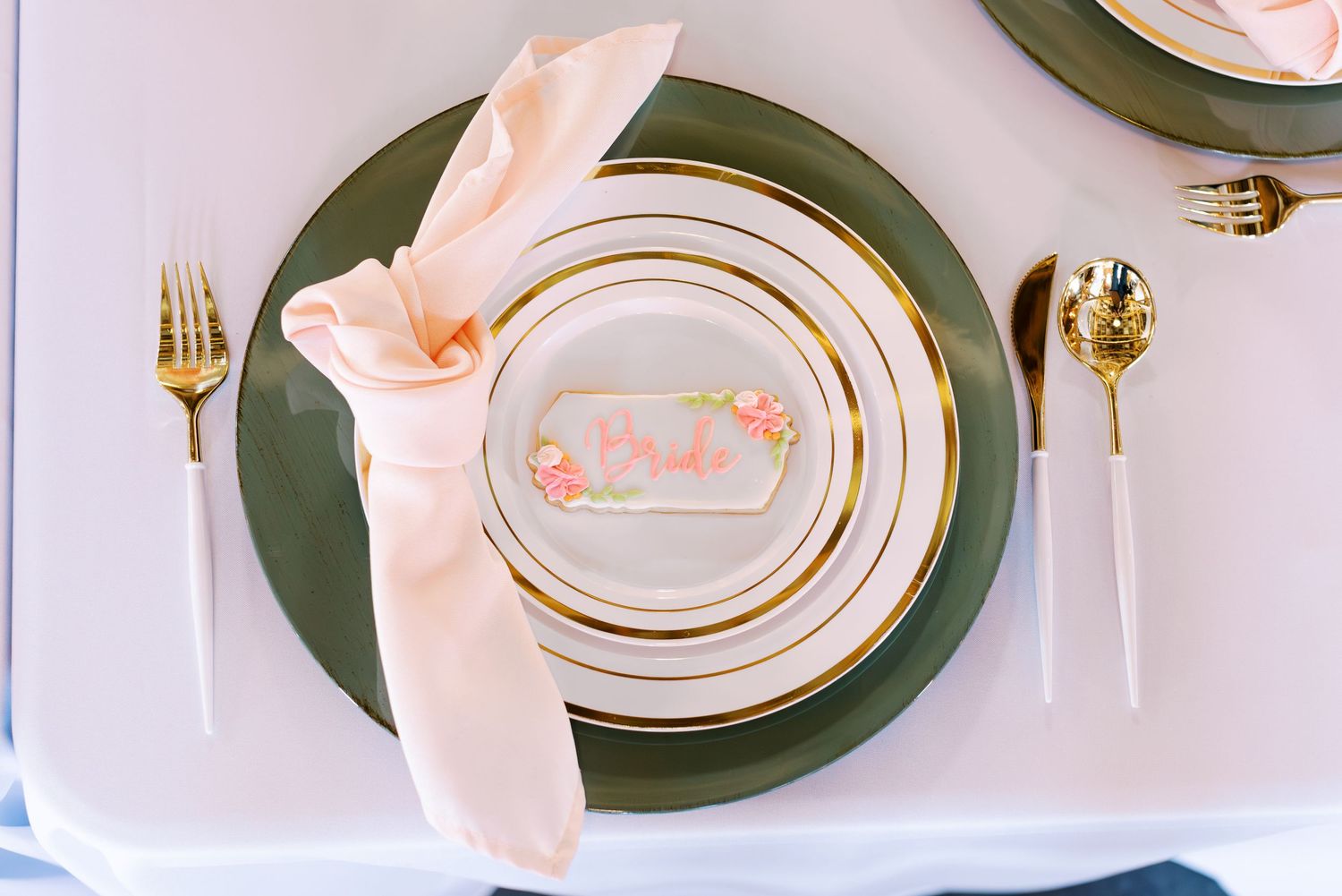 Elegant place setting with pink napkin and gold-rimmed plates for a wedding reception.