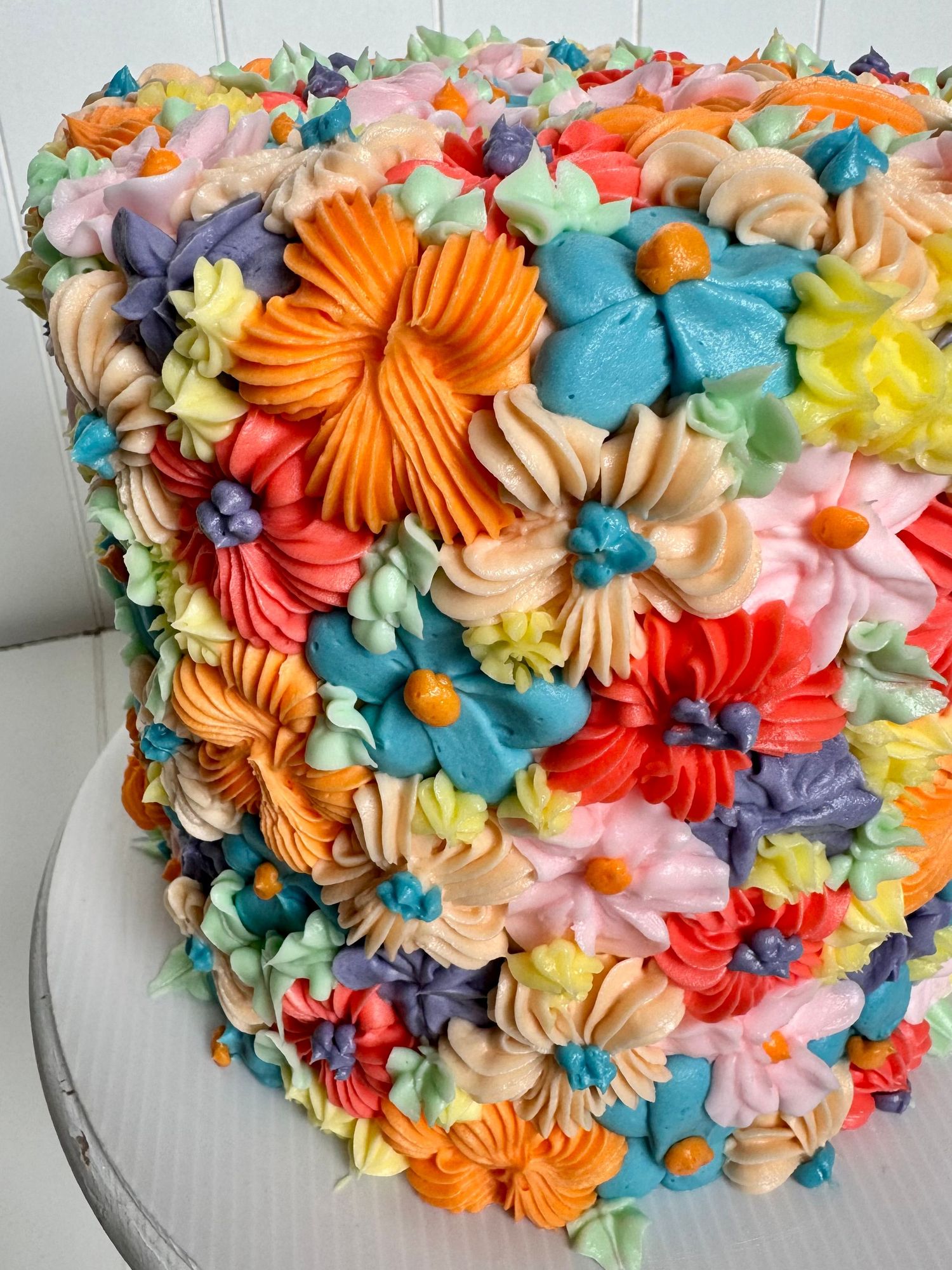 Colorful cake covered in vibrant piped buttercream flowers in rainbow hues.