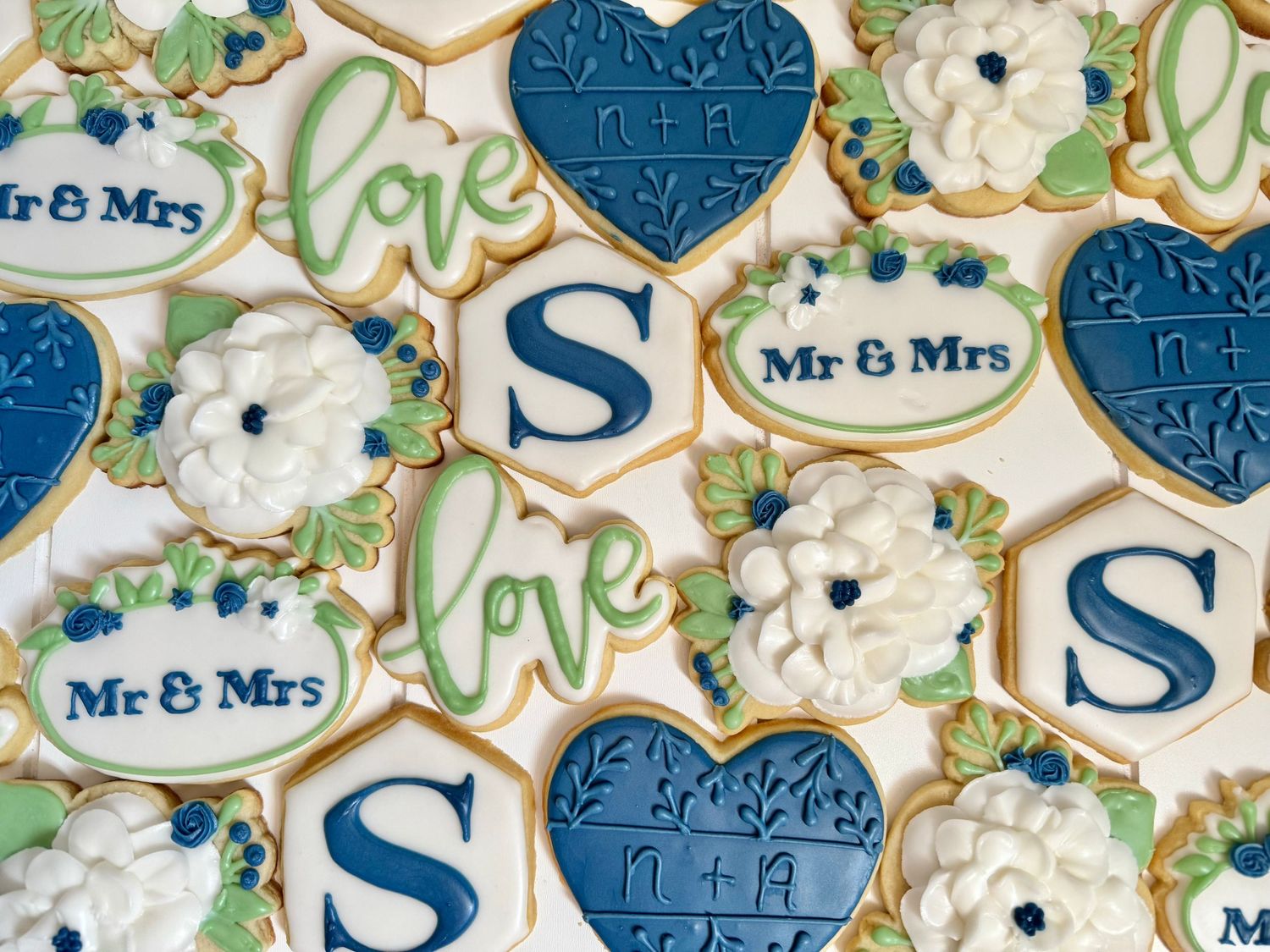 Wedding cookies decorated in blue and white with monograms and floral designs arranged in a pattern.