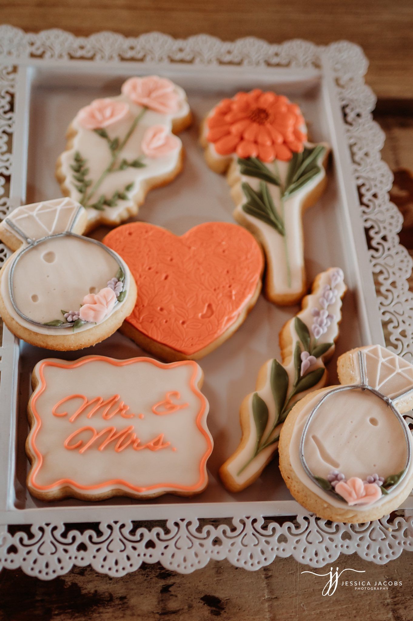 Elegant wedding cookies decorated in coral and white with delicate floral details displayed on white lace doilies.
