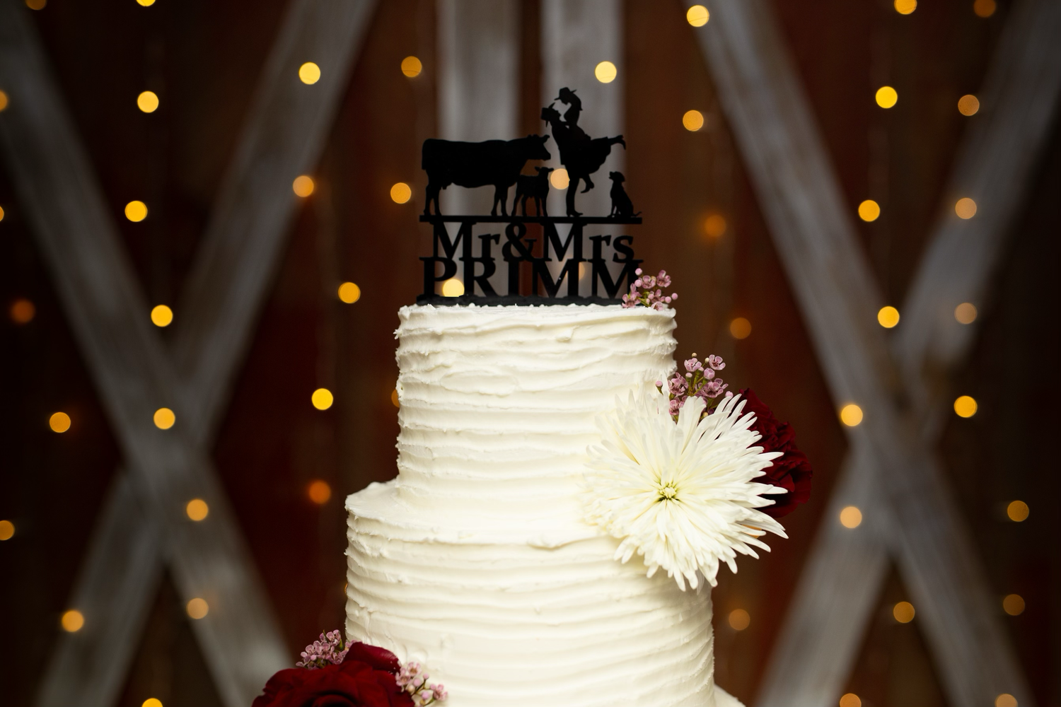 White textured wedding cake with delicate floral accents against a twinkling light backdrop.