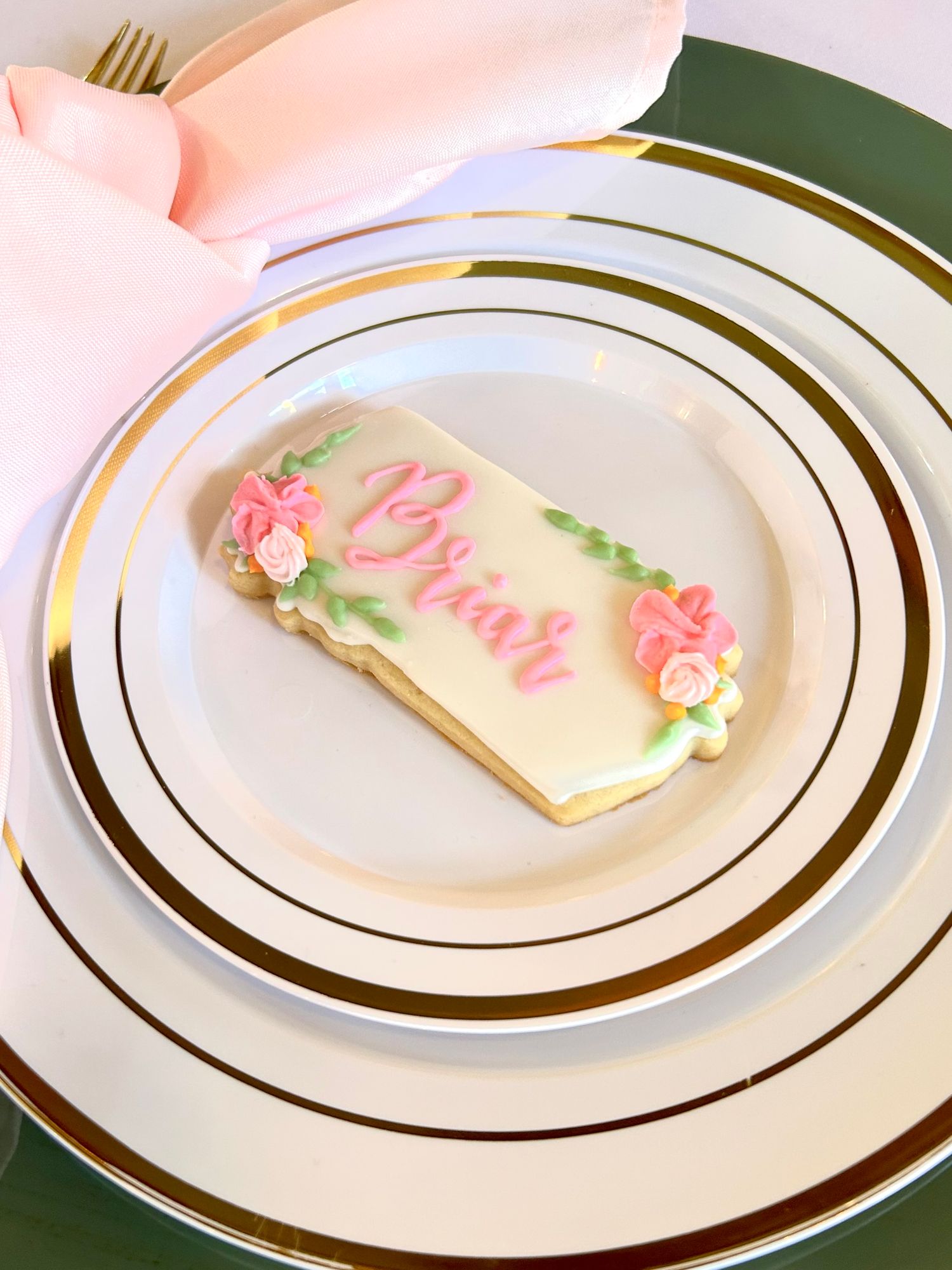 Elegant plated sugar cookie with pink floral accents on white and gold rimmed china.