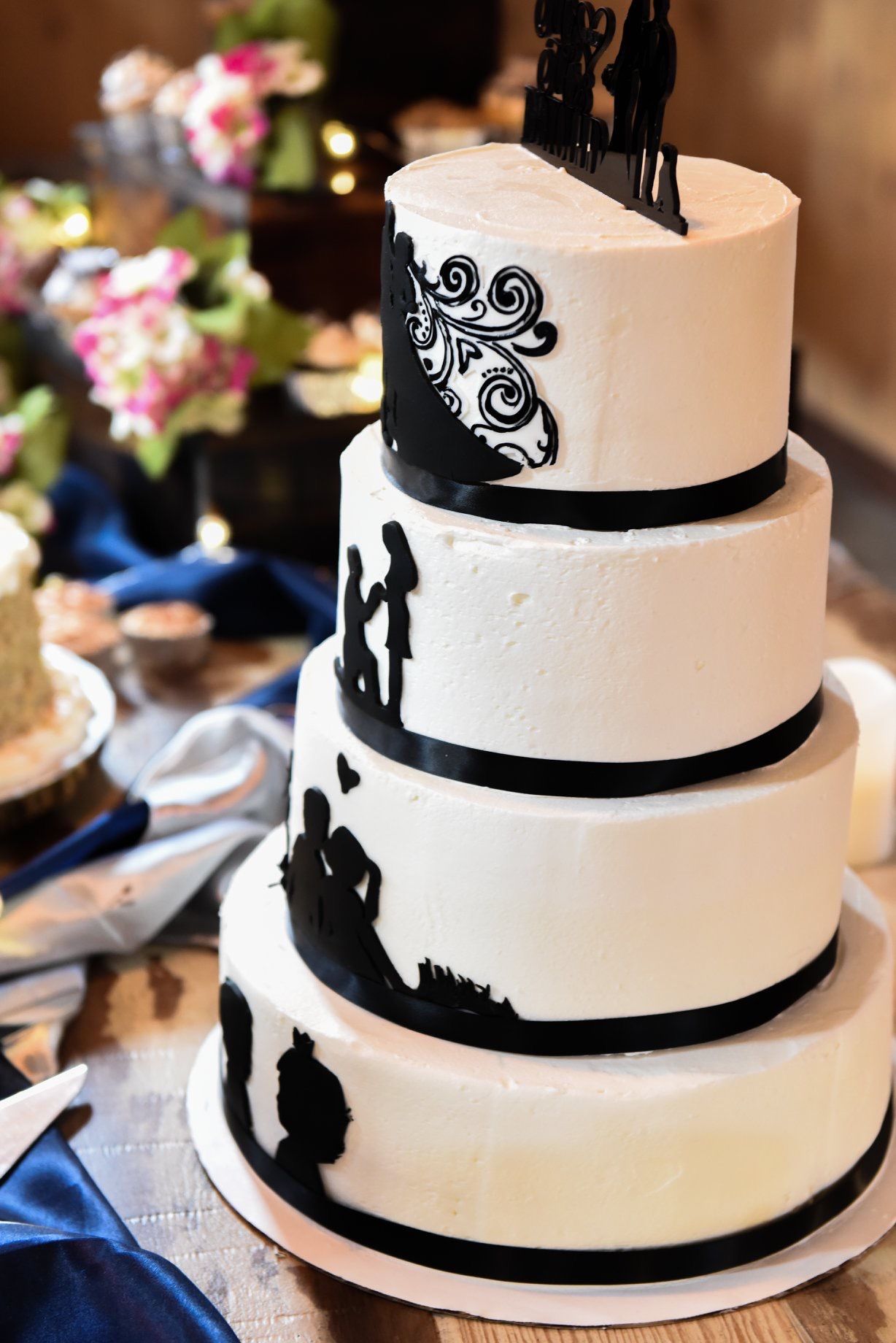 Three-tiered black and white wedding cake featuring elegant silhouette designs and scrollwork patterns.