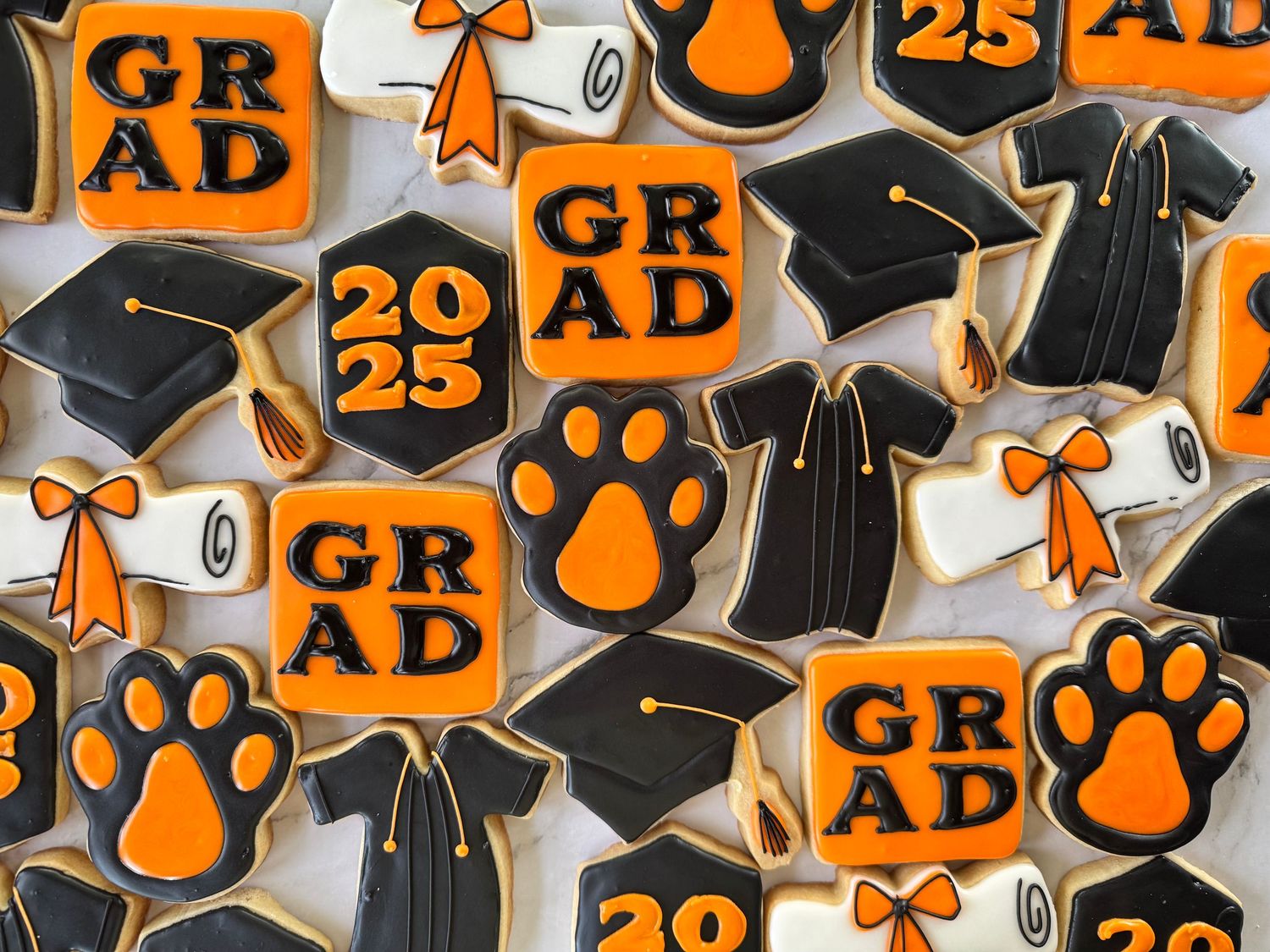 Graduation themed sugar cookies with orange and black designs including diplomas and paw prints.