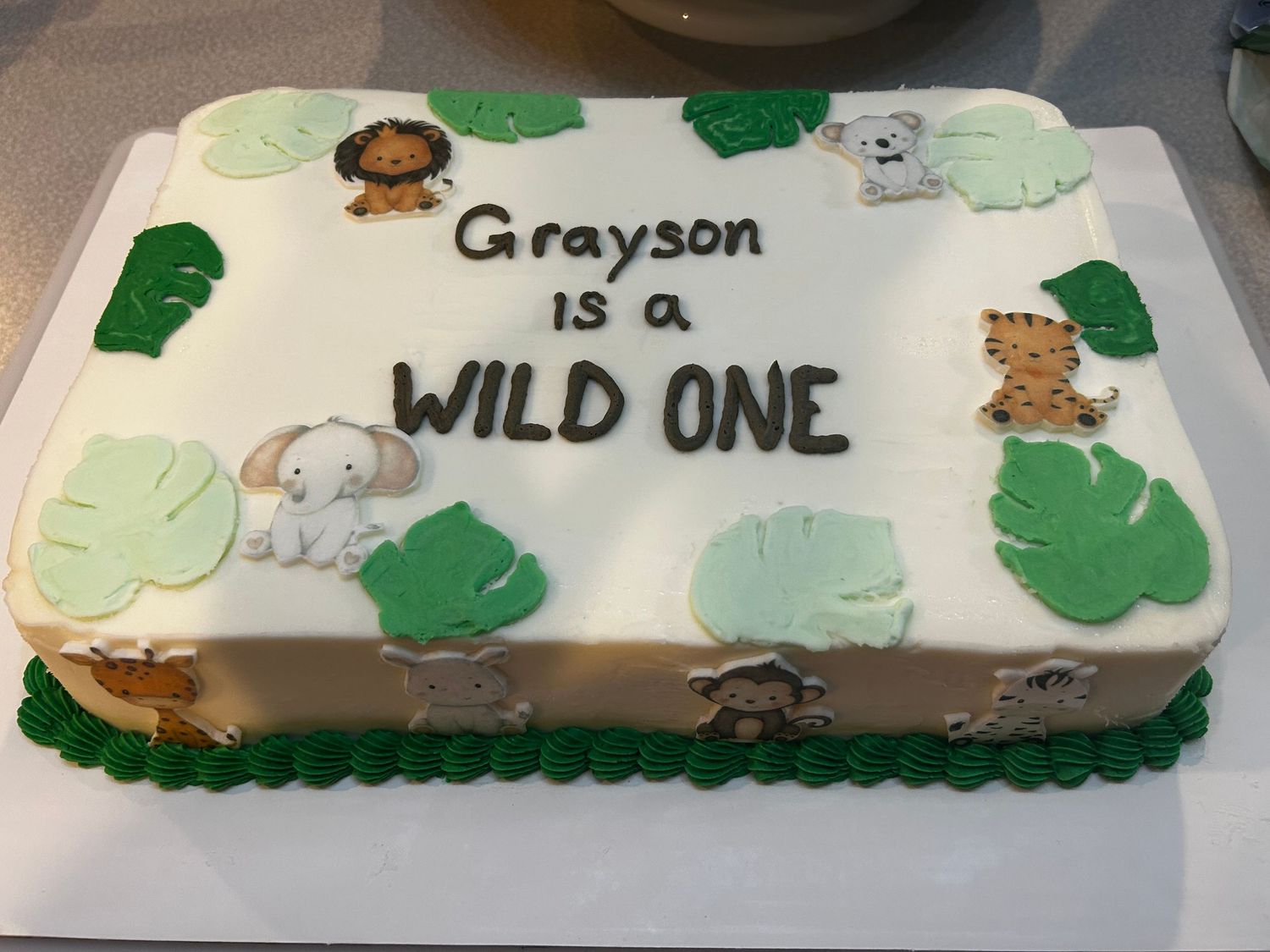 Safari themed sheet cake with jungle animals and green leaf decorations.