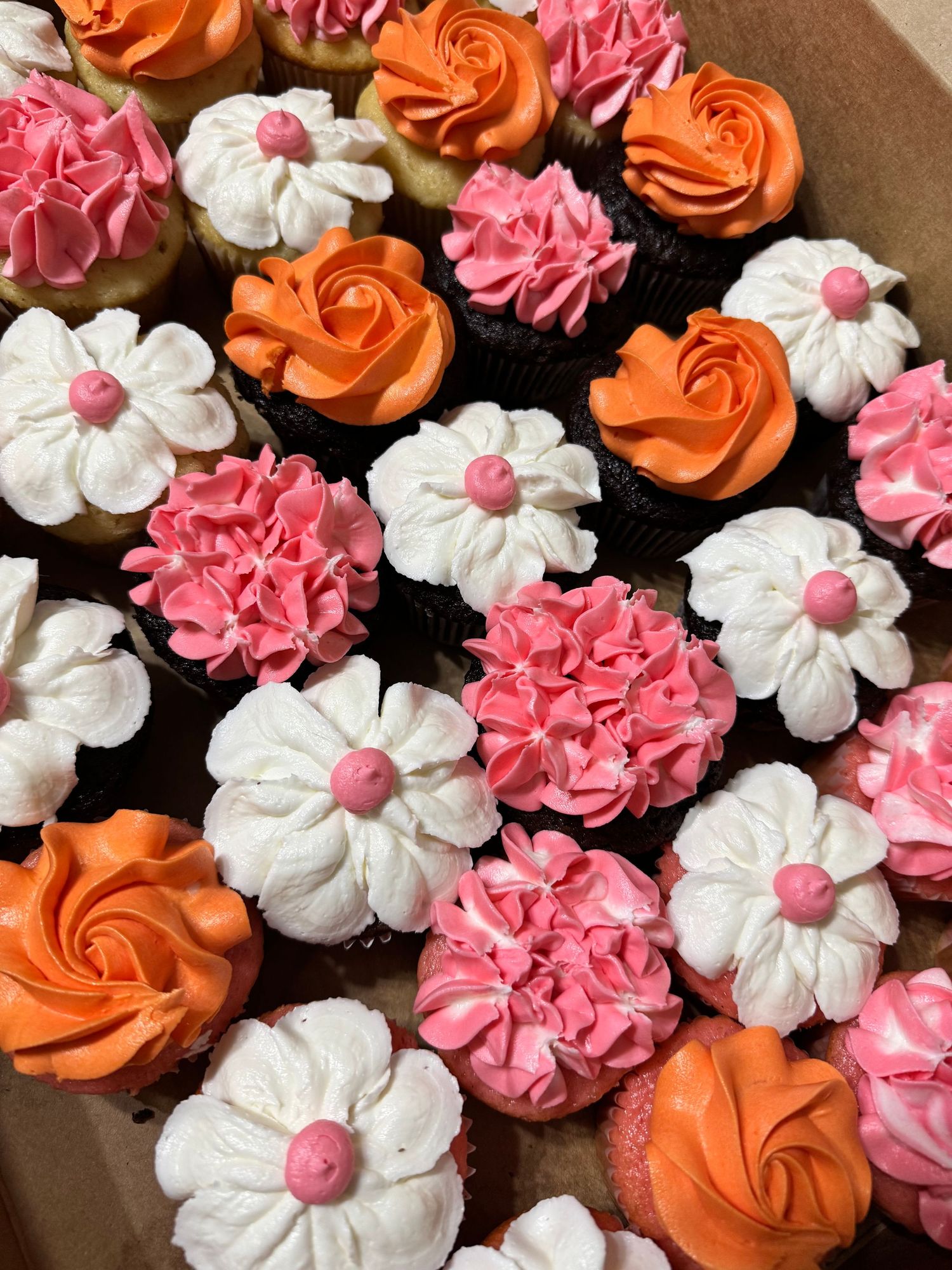 Cupcakes decorated with pink, orange and white flower-shaped frosting designs.