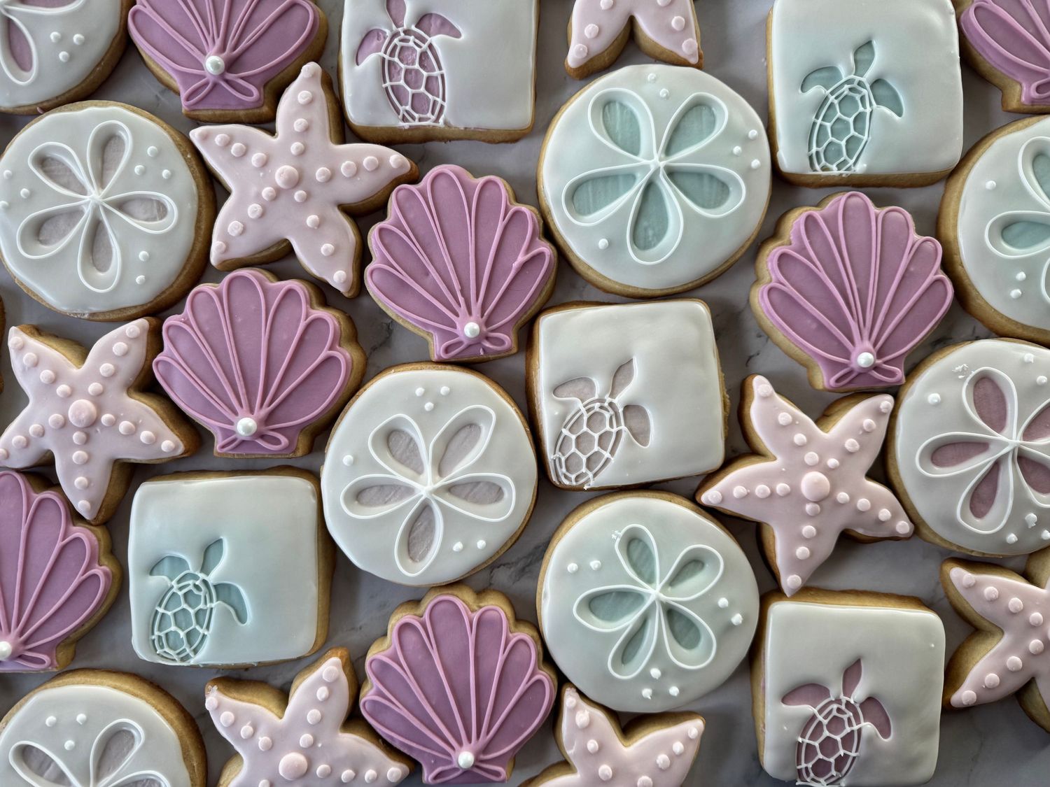 Decorated sugar cookies with purple and mint seashell designs and sand dollar patterns.