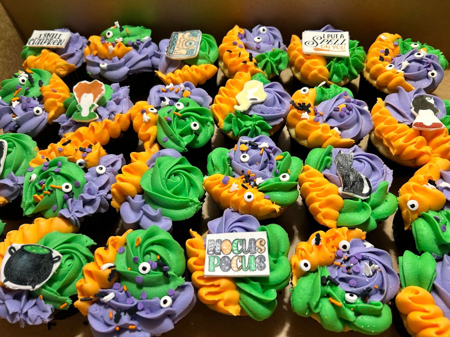 Colorful dinosaur themed cupcakes decorated with orange, green and purple frosting arranged in rows.