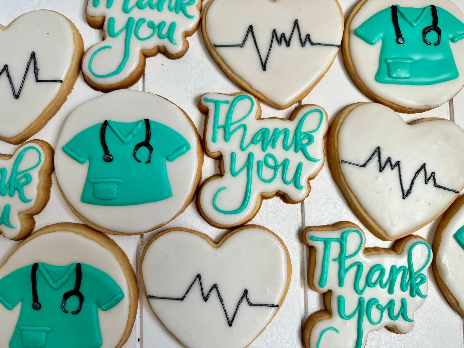 Medical themed sugar cookies decorated in teal with scrubs, heartbeat lines, and thank you messages.