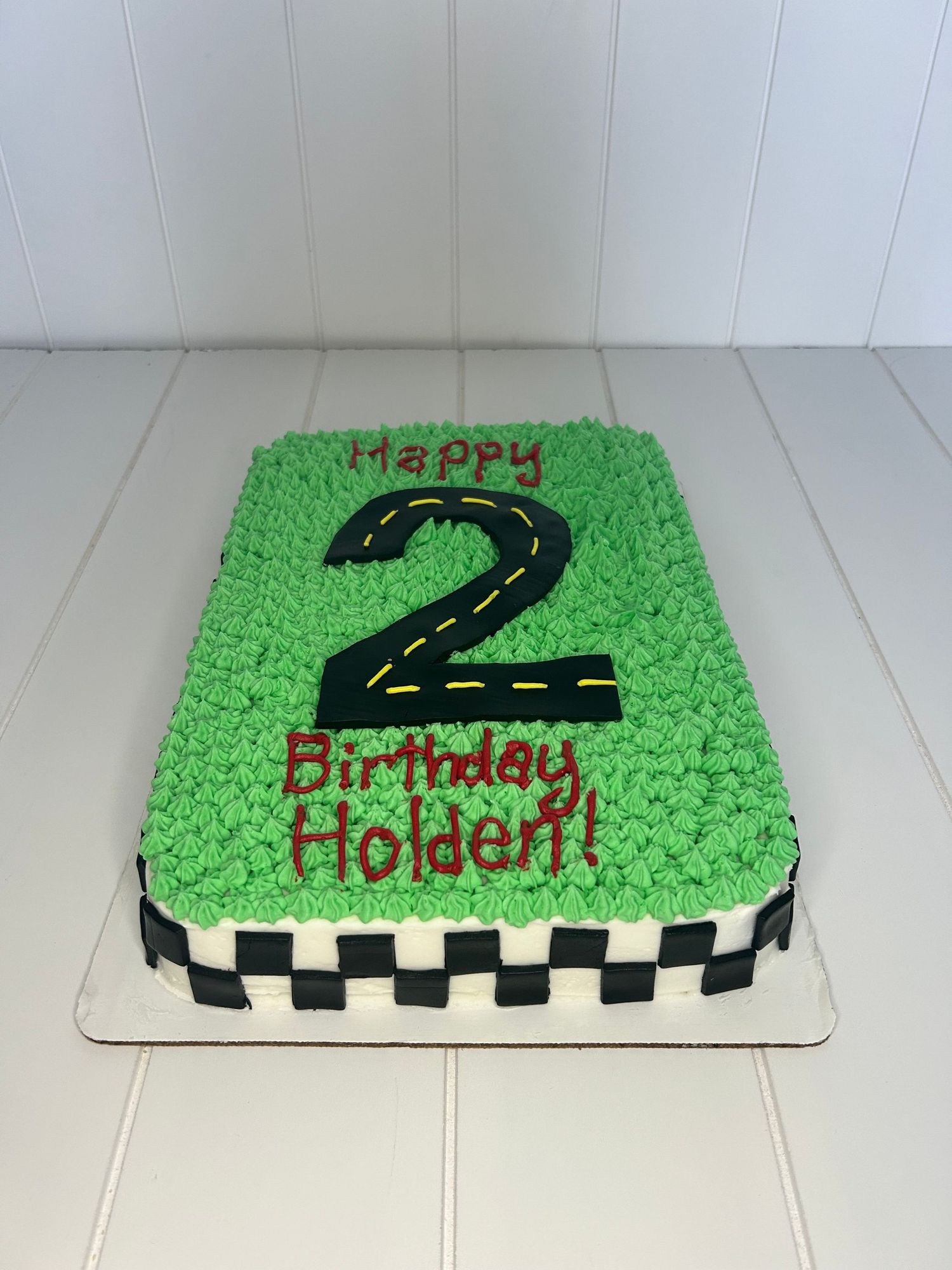 A green birthday cake shaped like the number 2 with a checkered border pattern.