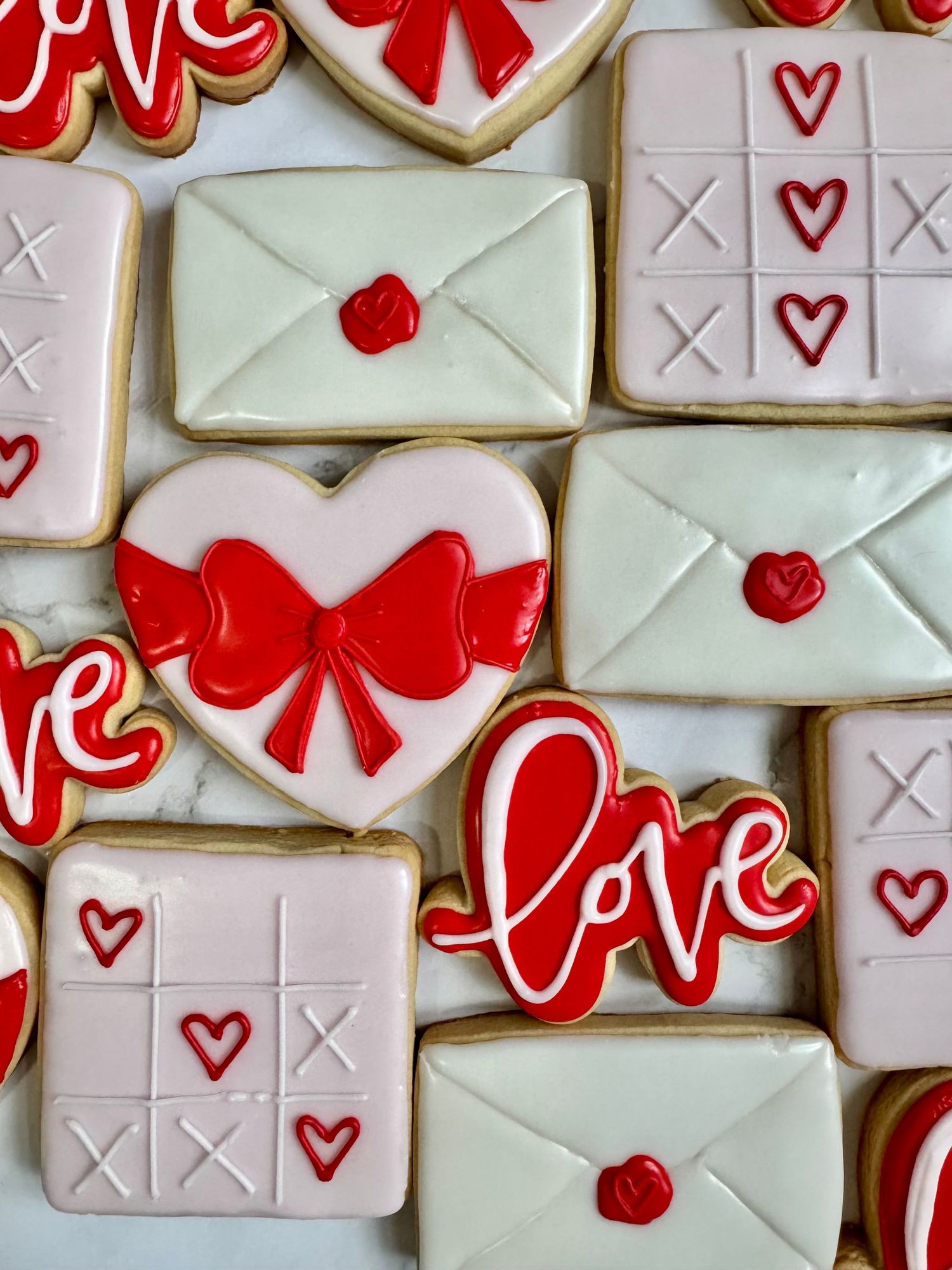 Valentine's day sugar cookies decorated with red bows, hearts, and love letters in white and red icing.