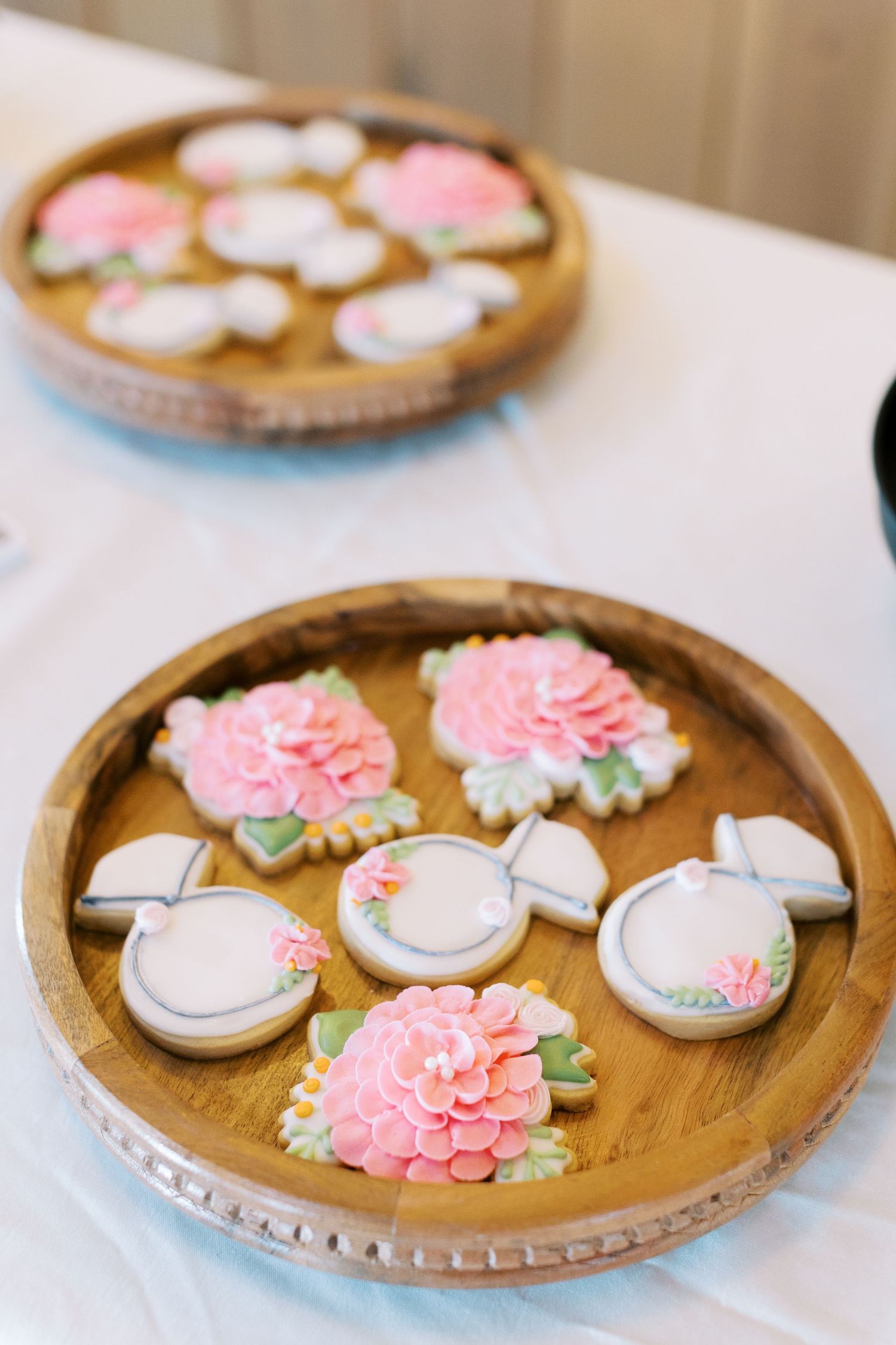 Rustic wooden tray displaying delicate wedding cookies with pink floral decorations.